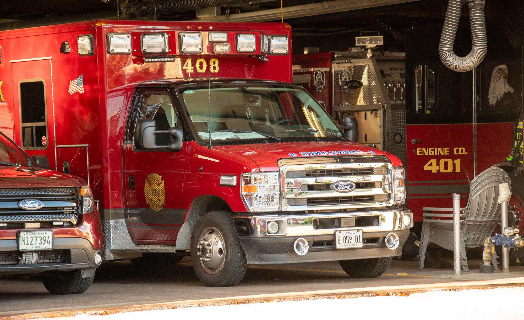 Red ambulance and fire engine parked inside a fire station bay.