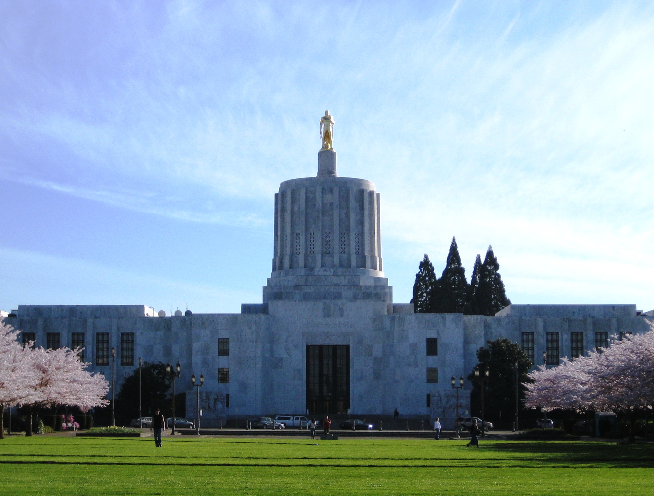 Front exterior of the Oregon State Capitol building with cherry trees in bloom on either side.