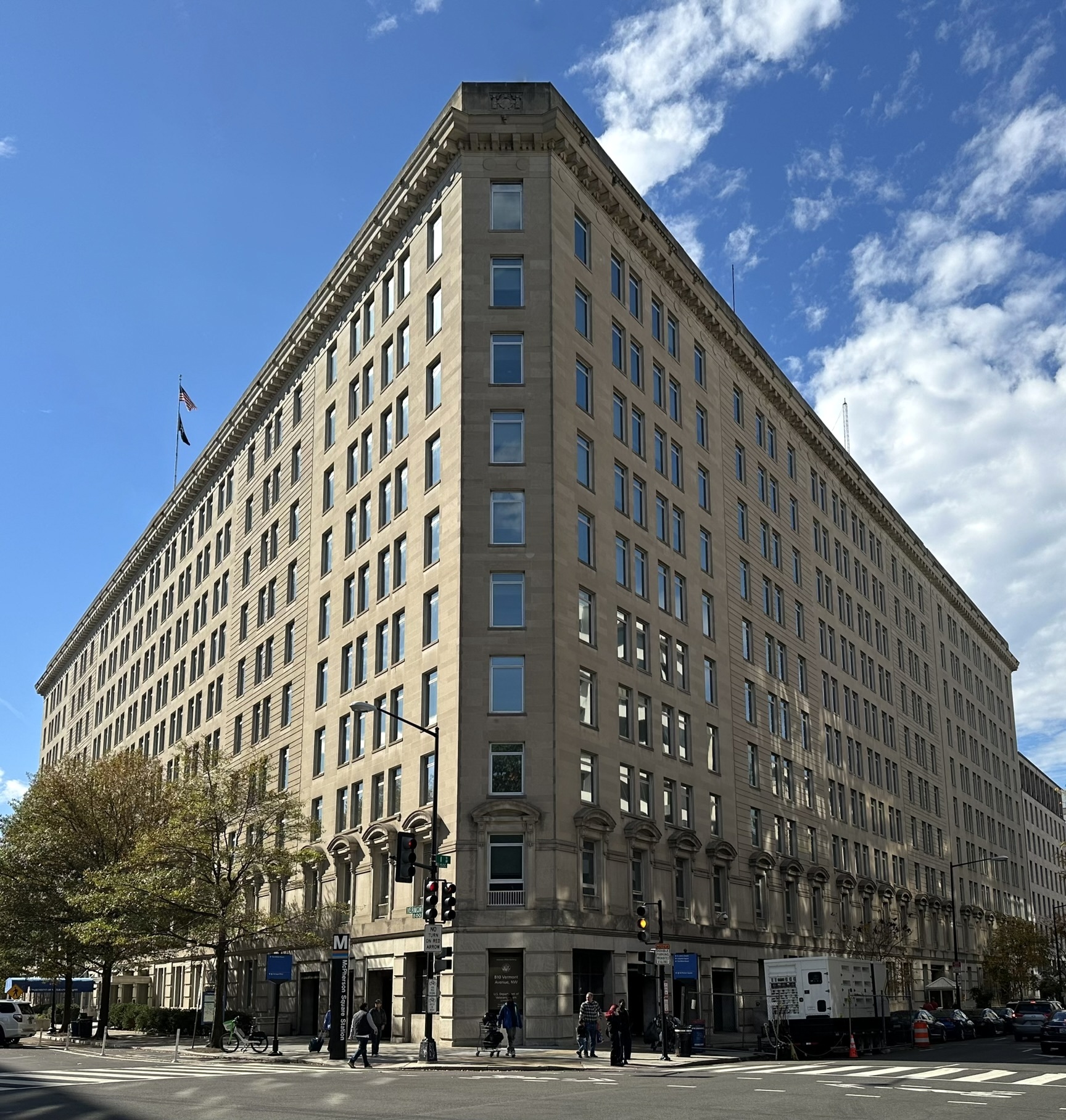 Large neoclassical stone government building on a city street corner with an American flag flying from the roof.
