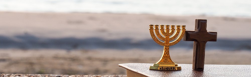 A gold menorah and a wooden cross placed side by side on a surface.