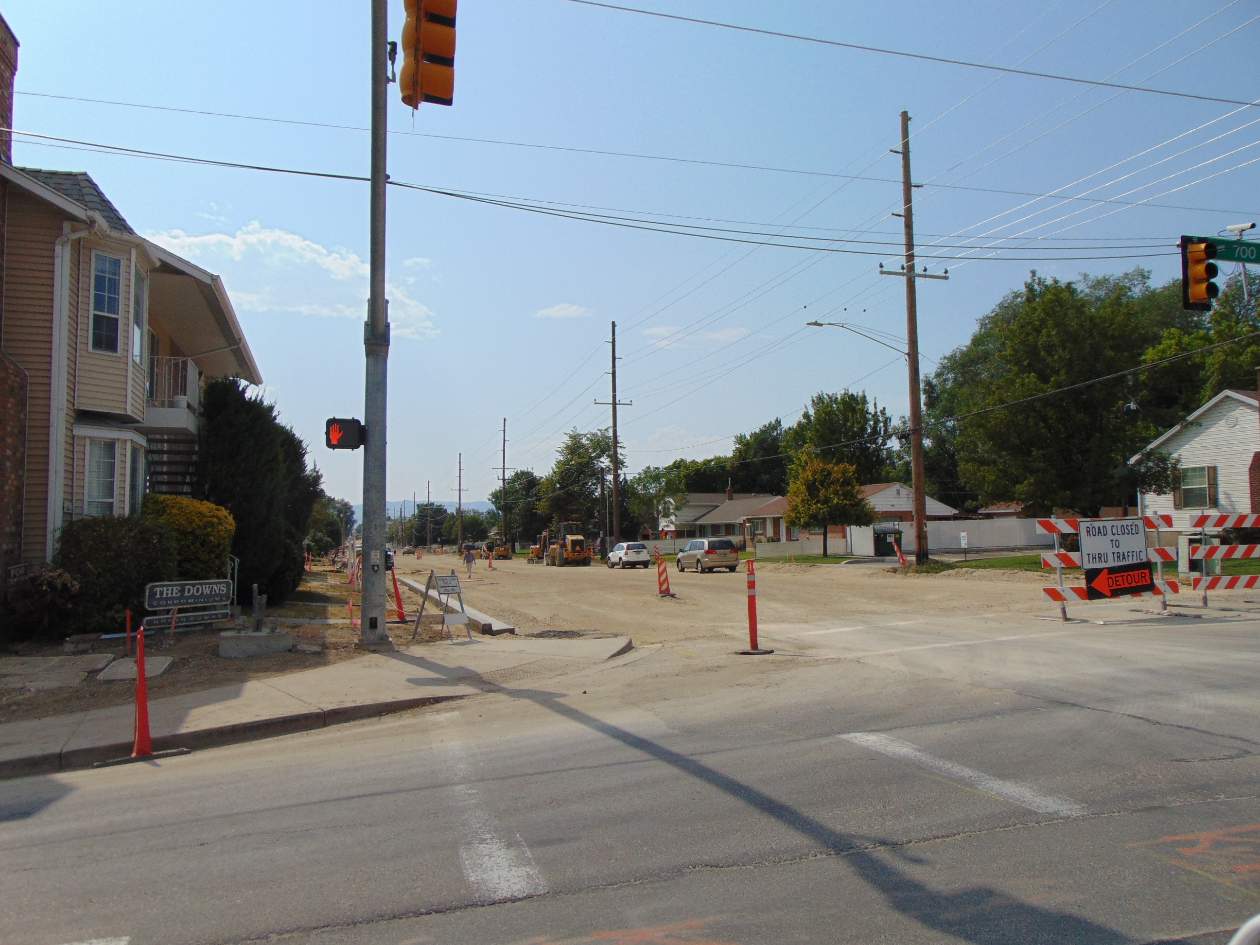 Orange construction barricades block a street intersection with a detour sign on the right.