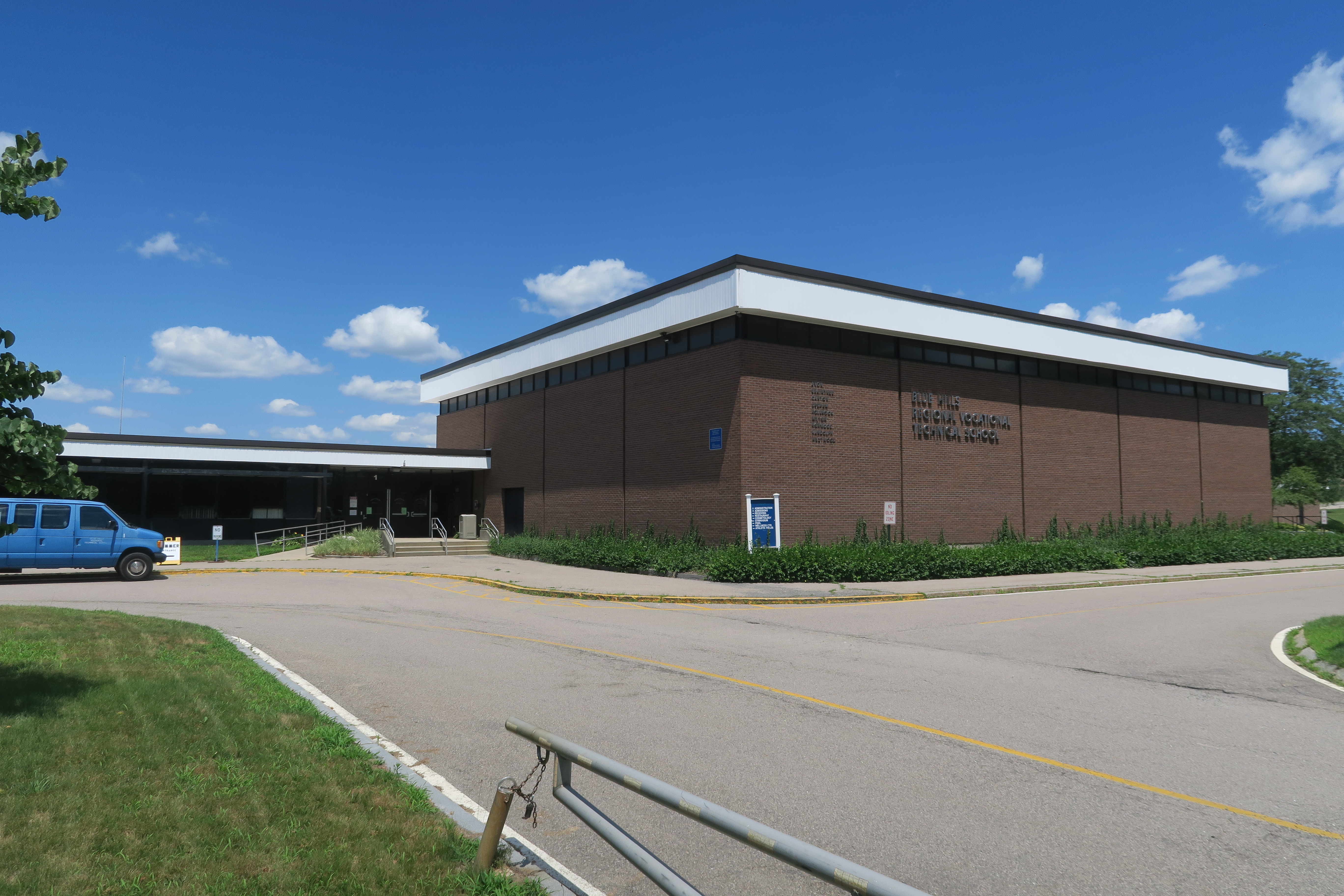 Single-story brick school building with flat roof and parking lot under a blue sky.