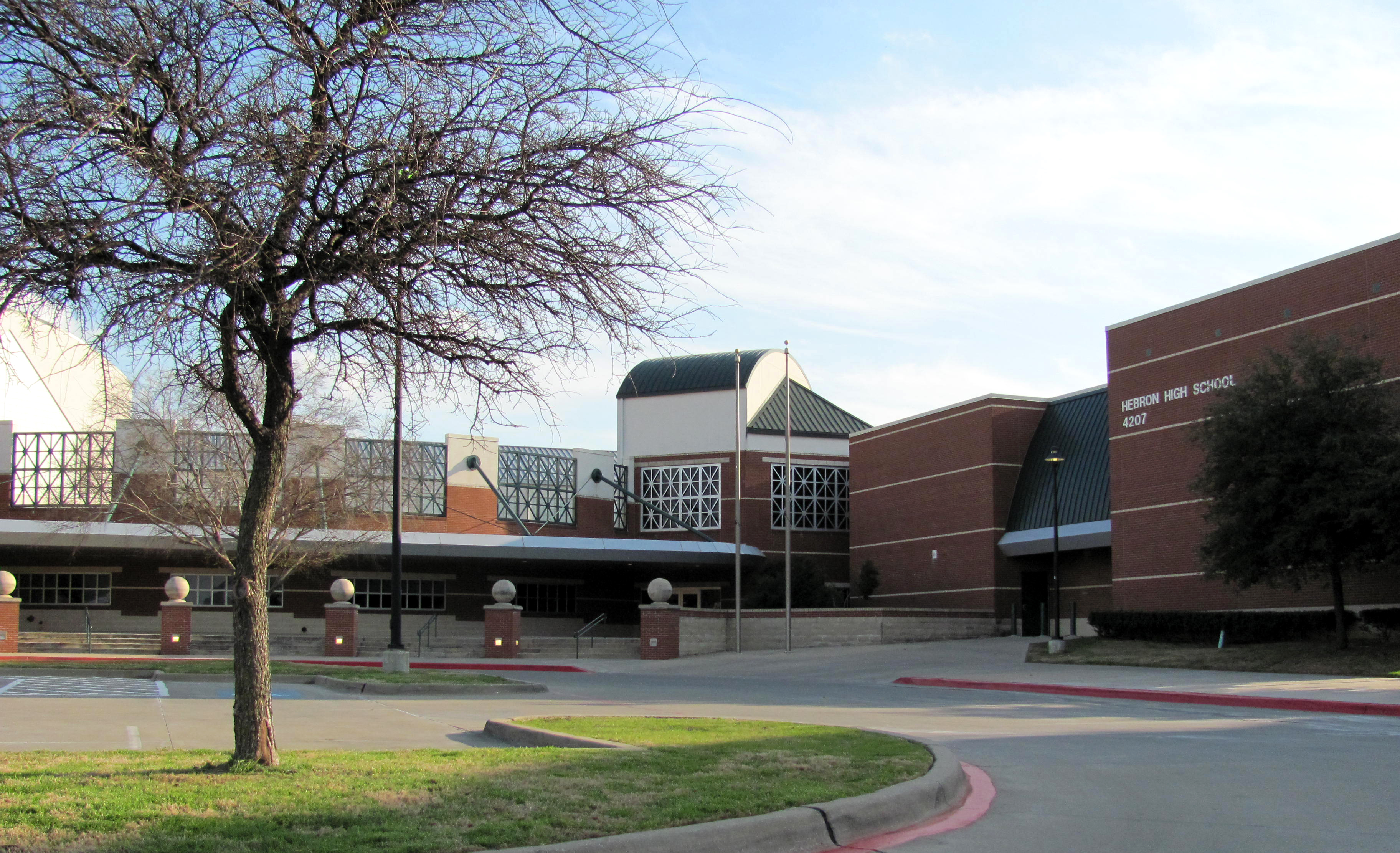 Brick front entrance of a high school with a covered walkway and bare tree.