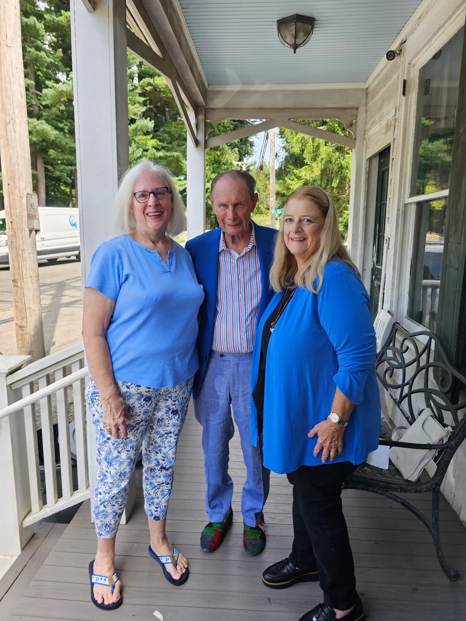 Three smiling people in blue clothing pose together on a wooden covered porch.