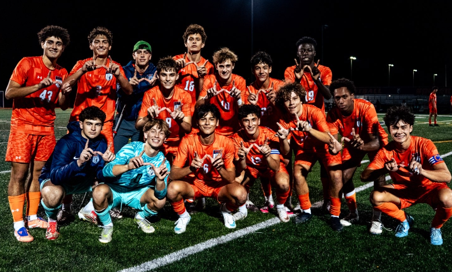 Soccer players in orange uniforms pose together on a lit field at night.