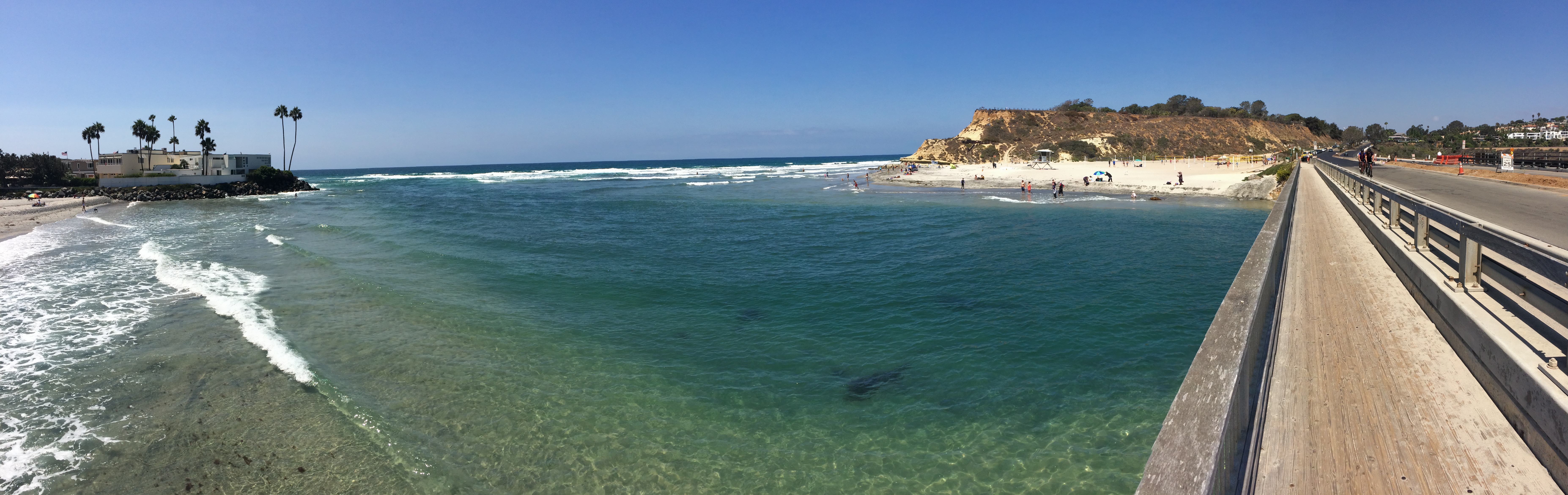 Panoramic view of a sunny Southern California beach with turquoise water and sandstone cliffs.