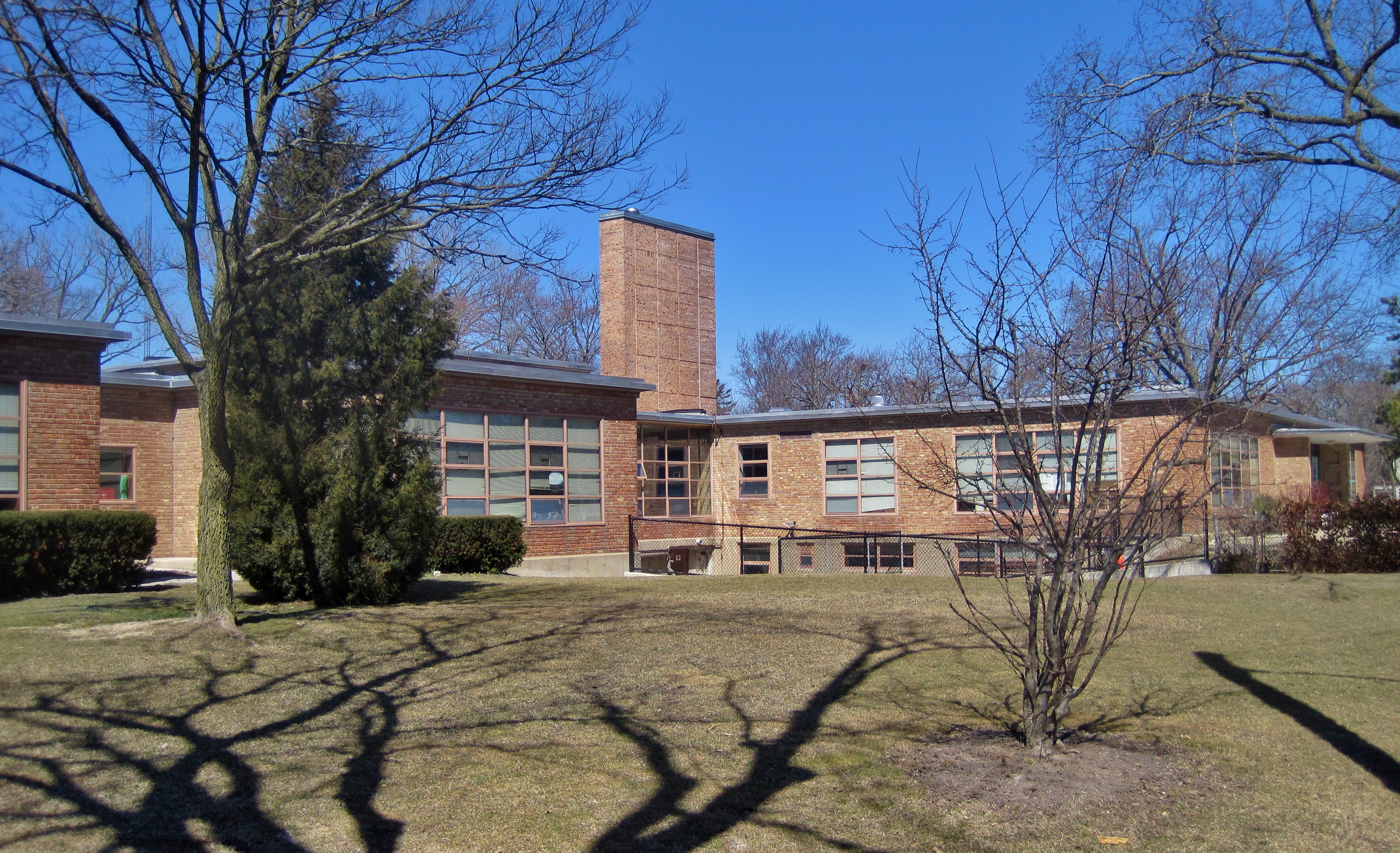 Single-story brick school building with tall chimney and bare trees on a clear day.