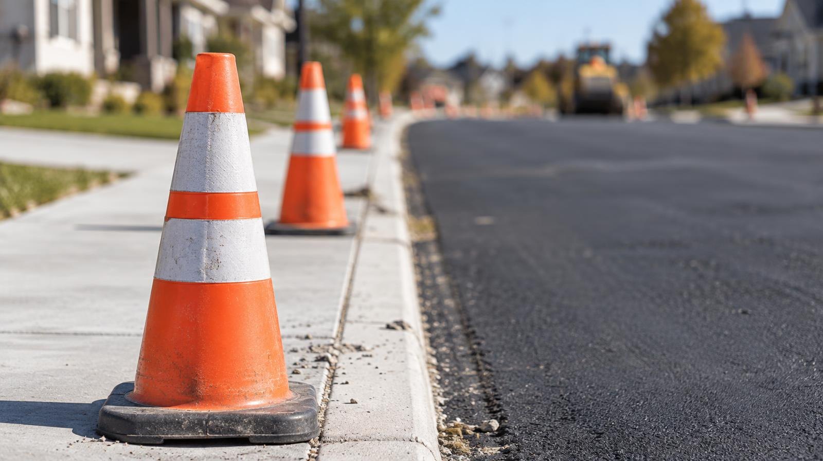 Freshly paved road with new sidewalks and orange construction cones along the curb.