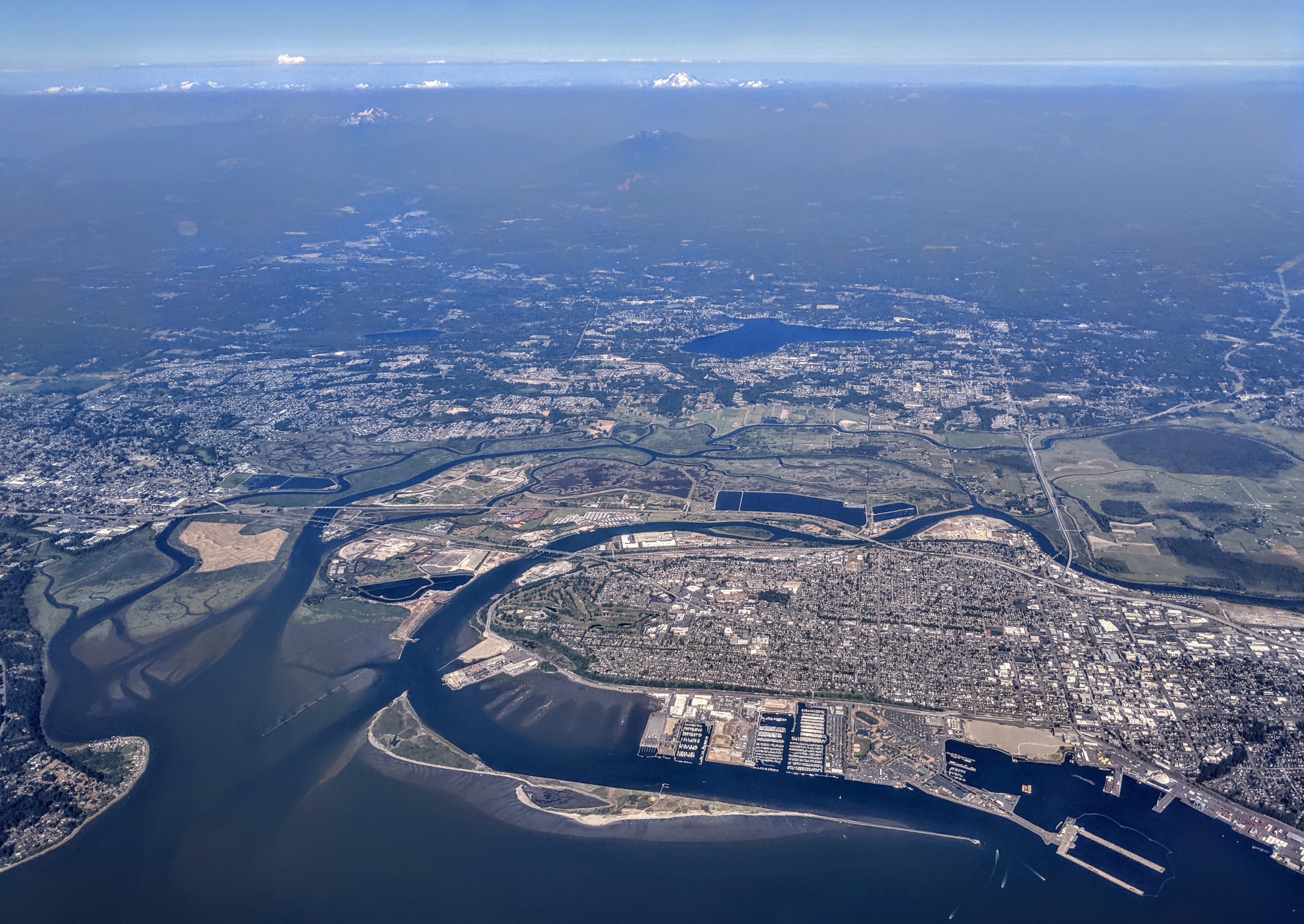 Aerial view of a city along a river, with an industrial port visible at lower right.
