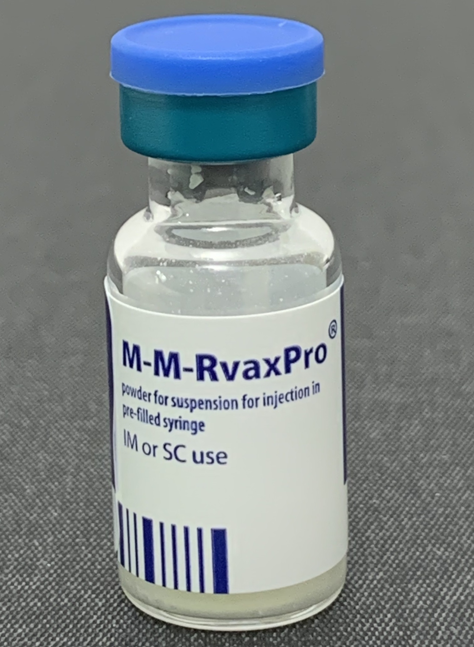 A glass vial of MMR vaccine with a blue cap on a gray surface.