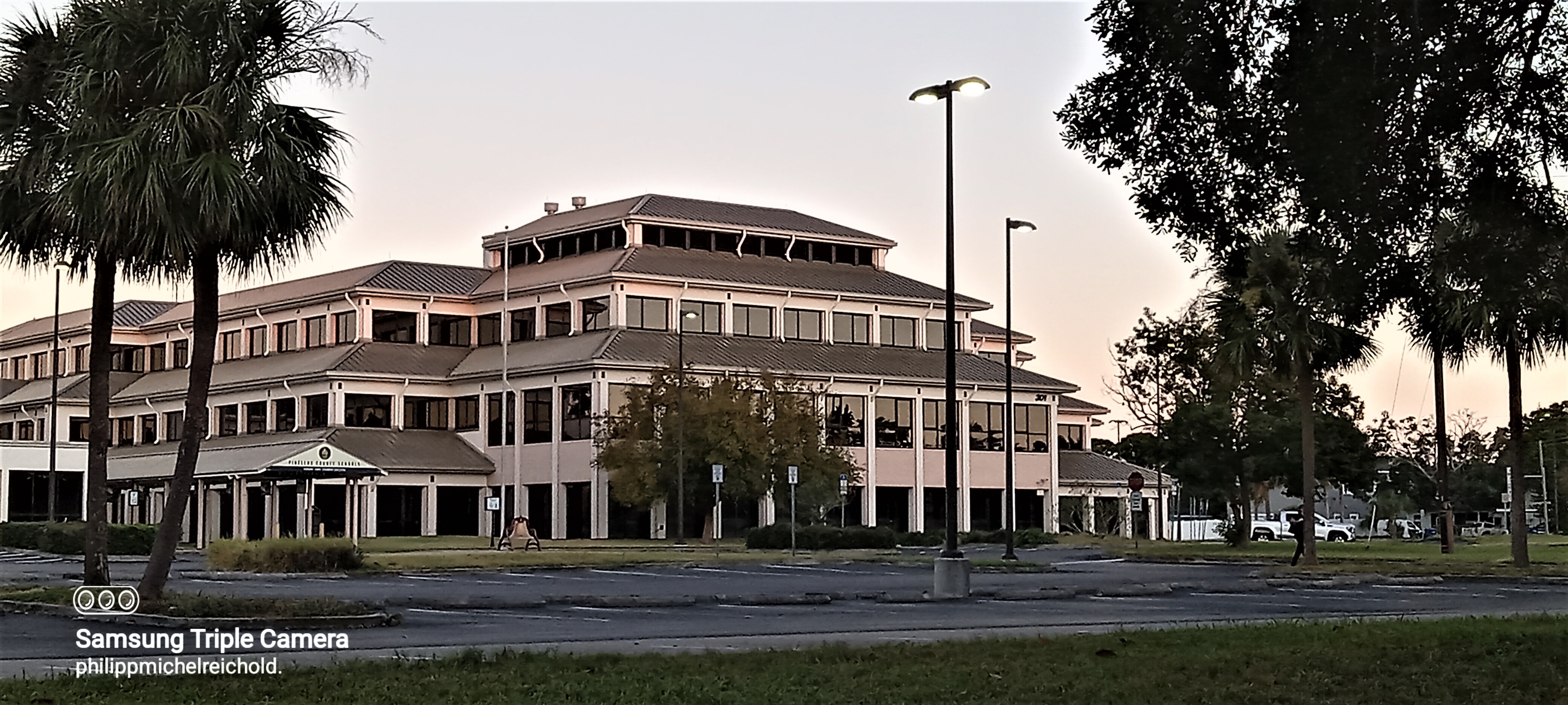 Multi-story beige office building with palm trees and street lamps in the foreground.