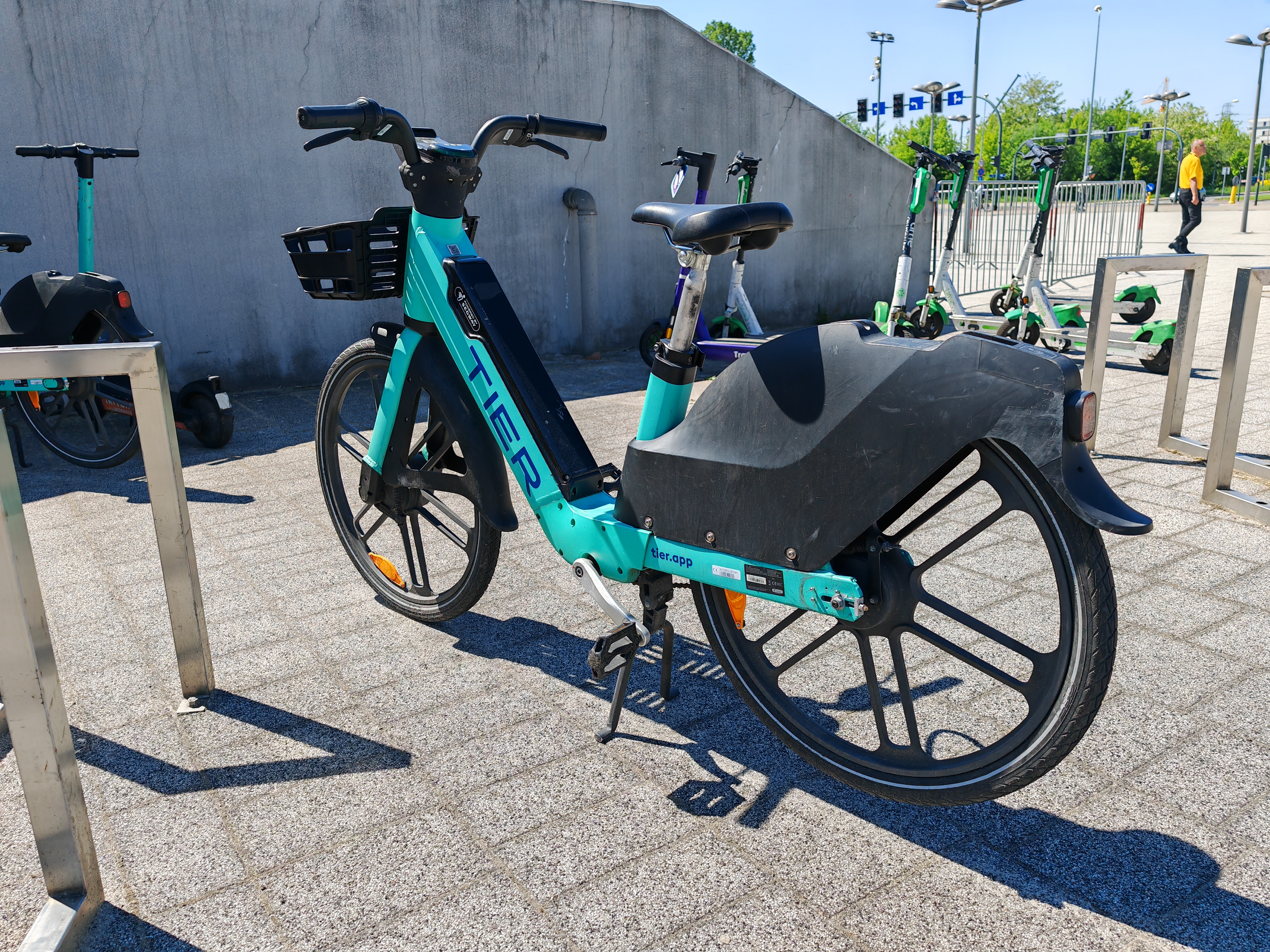 A teal electric bike parked outdoors with electric scooters visible in the background.