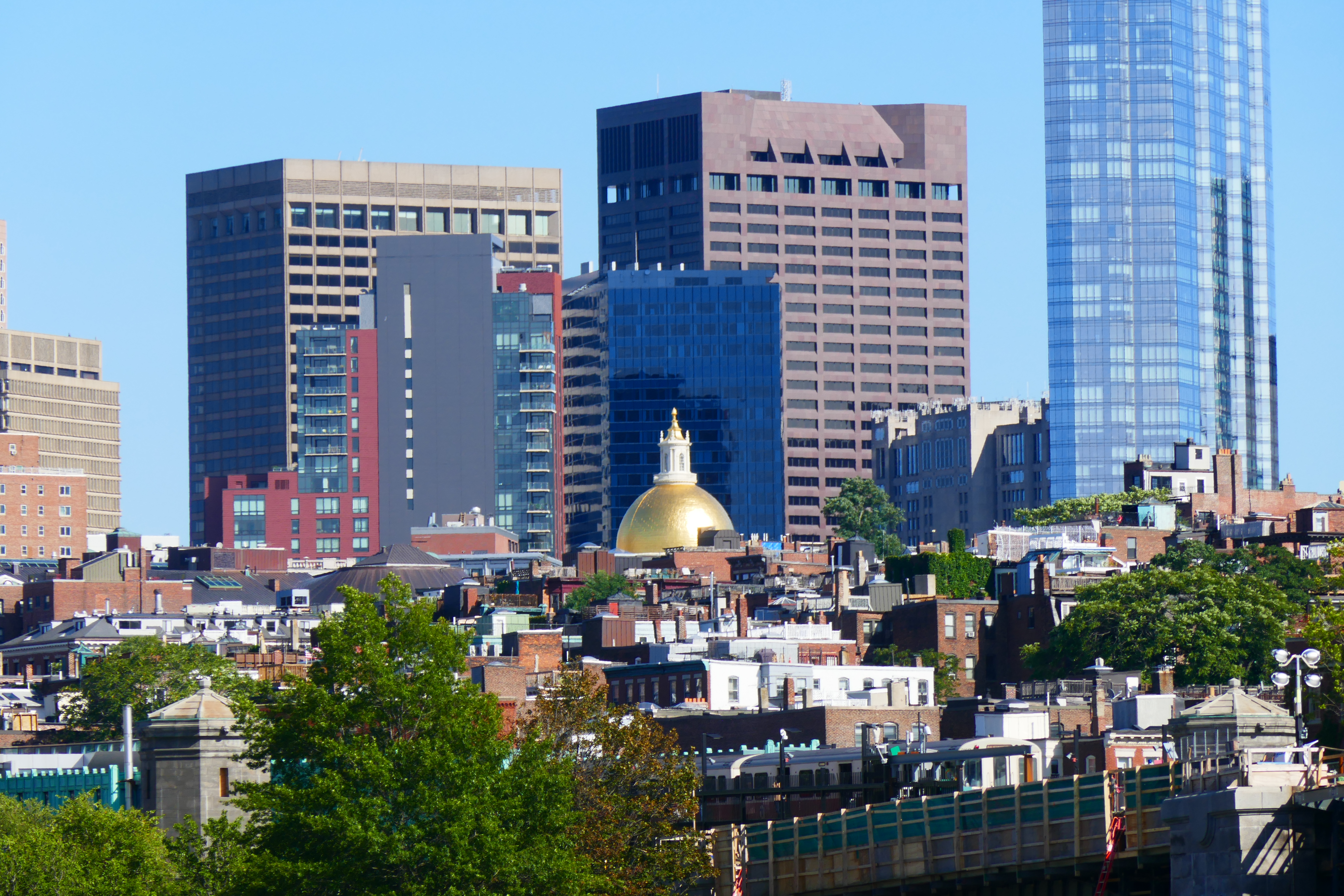 City skyline with a gold dome visible among rooftops and green trees in the foreground.