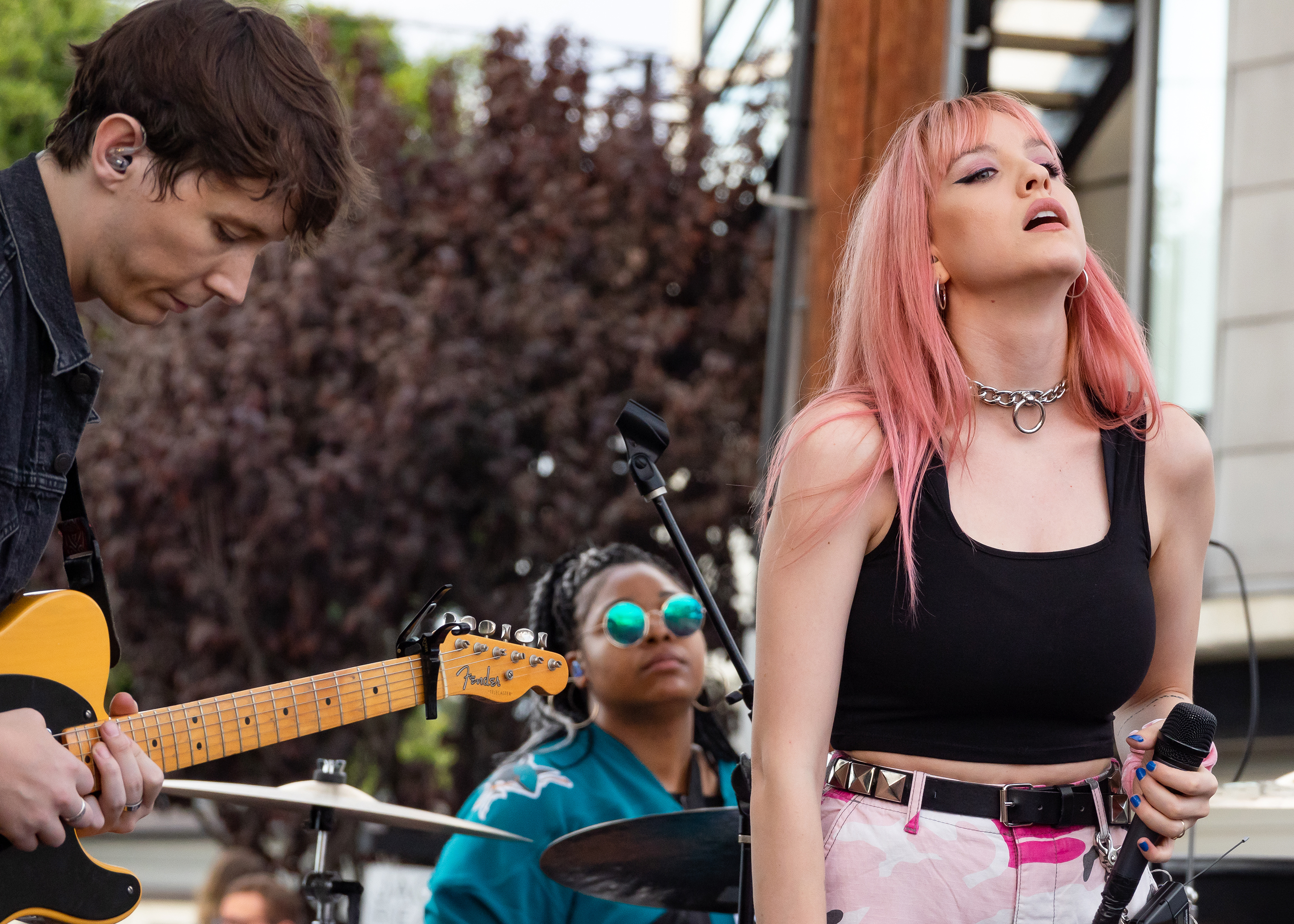 A band with a female singer and guitarist performs on an outdoor festival stage.