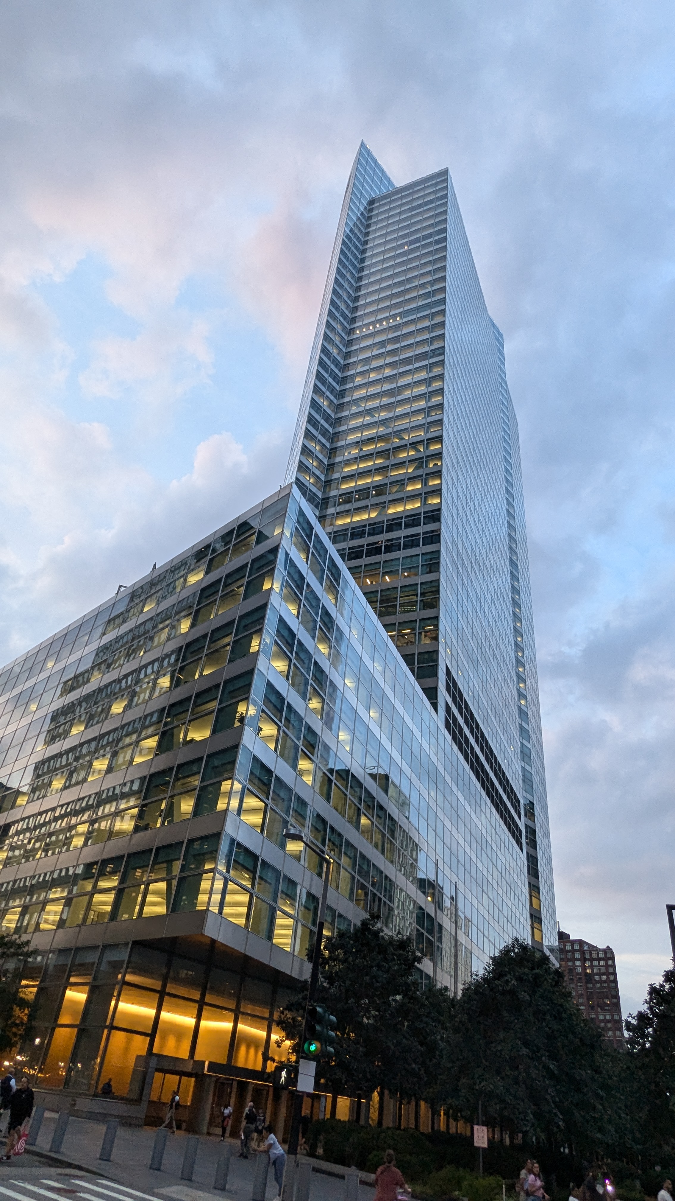Tall glass skyscraper with lit windows photographed from street level at dusk.