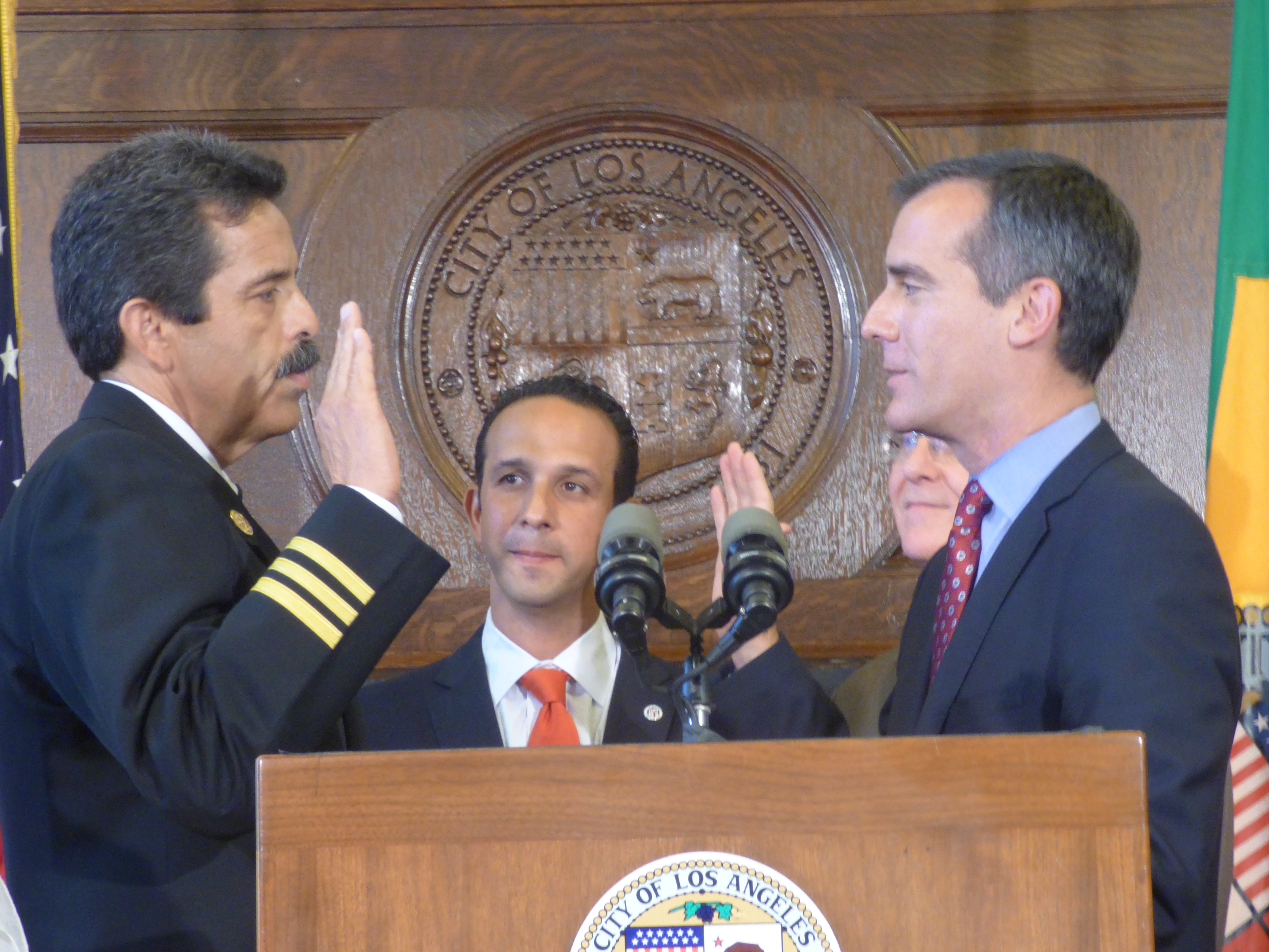 Uniformed fire official raises right hand taking an oath before another official indoors.