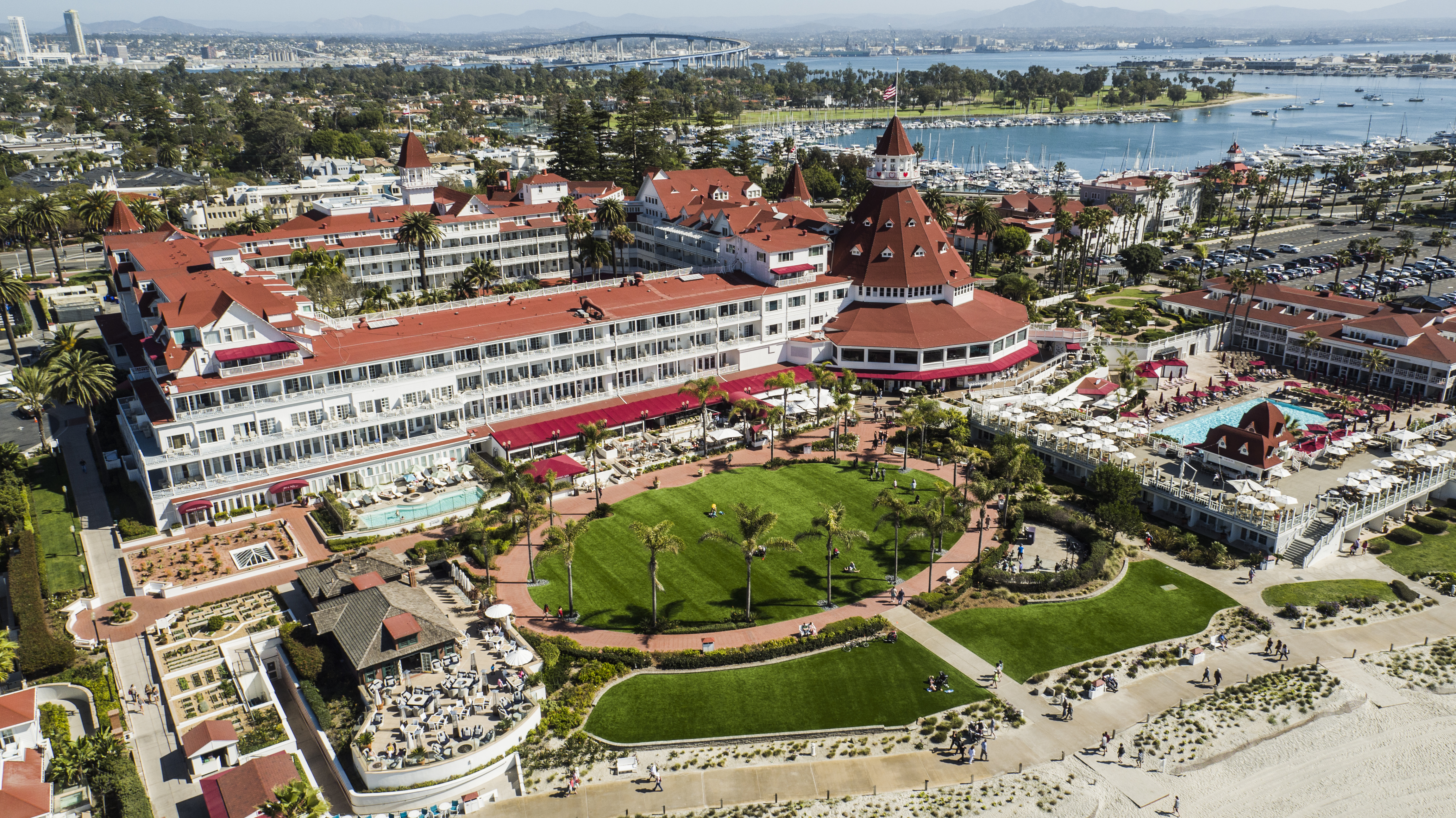 Aerial view of a red-roofed Victorian resort complex next to a sandy beach.