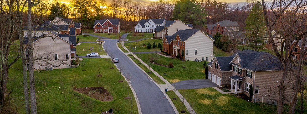Aerial drone view of a suburban neighborhood with homes along a winding road at sunset.
