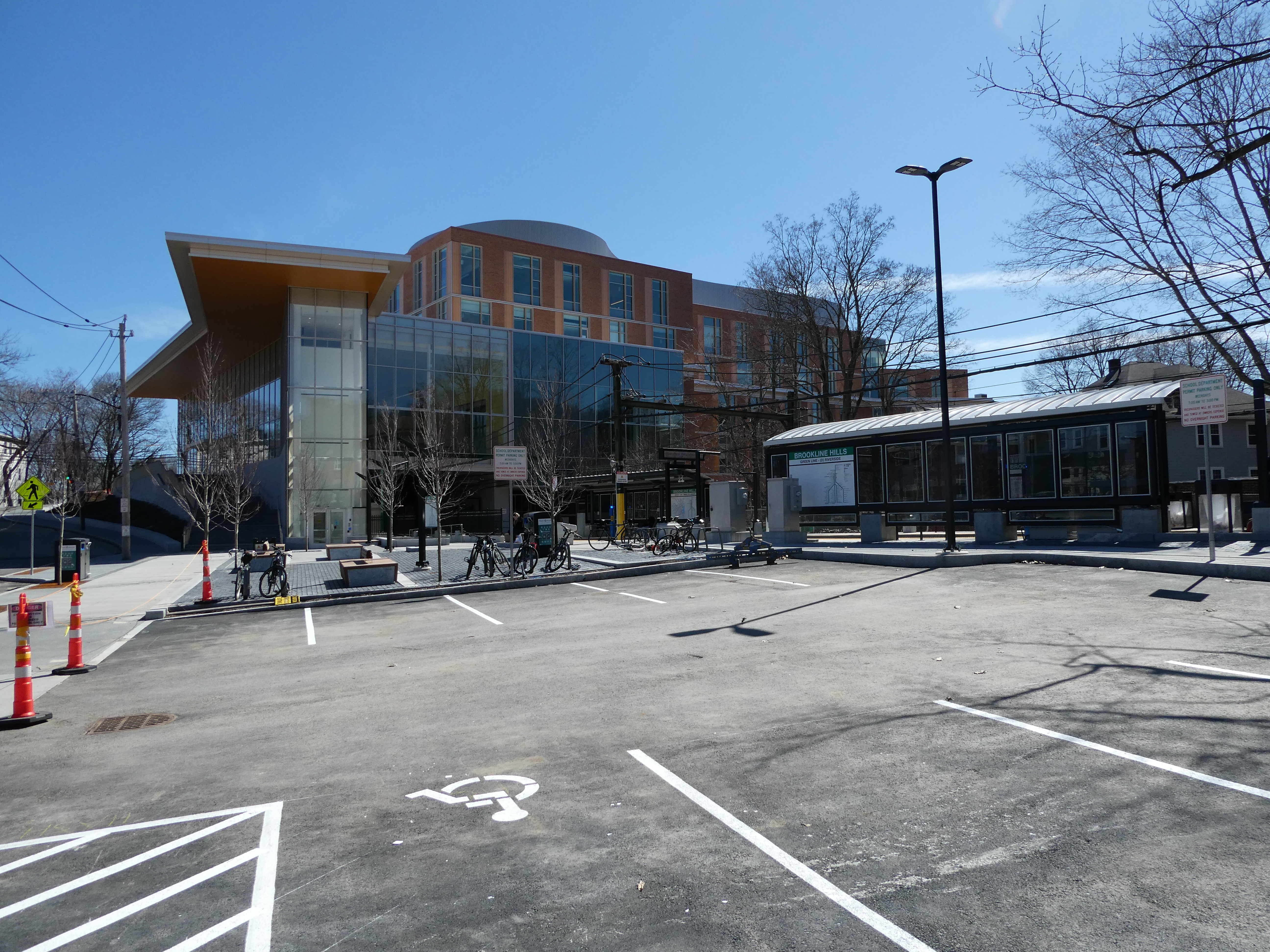Modern glass-and-brick school building behind a parking lot under a clear blue sky with bare trees