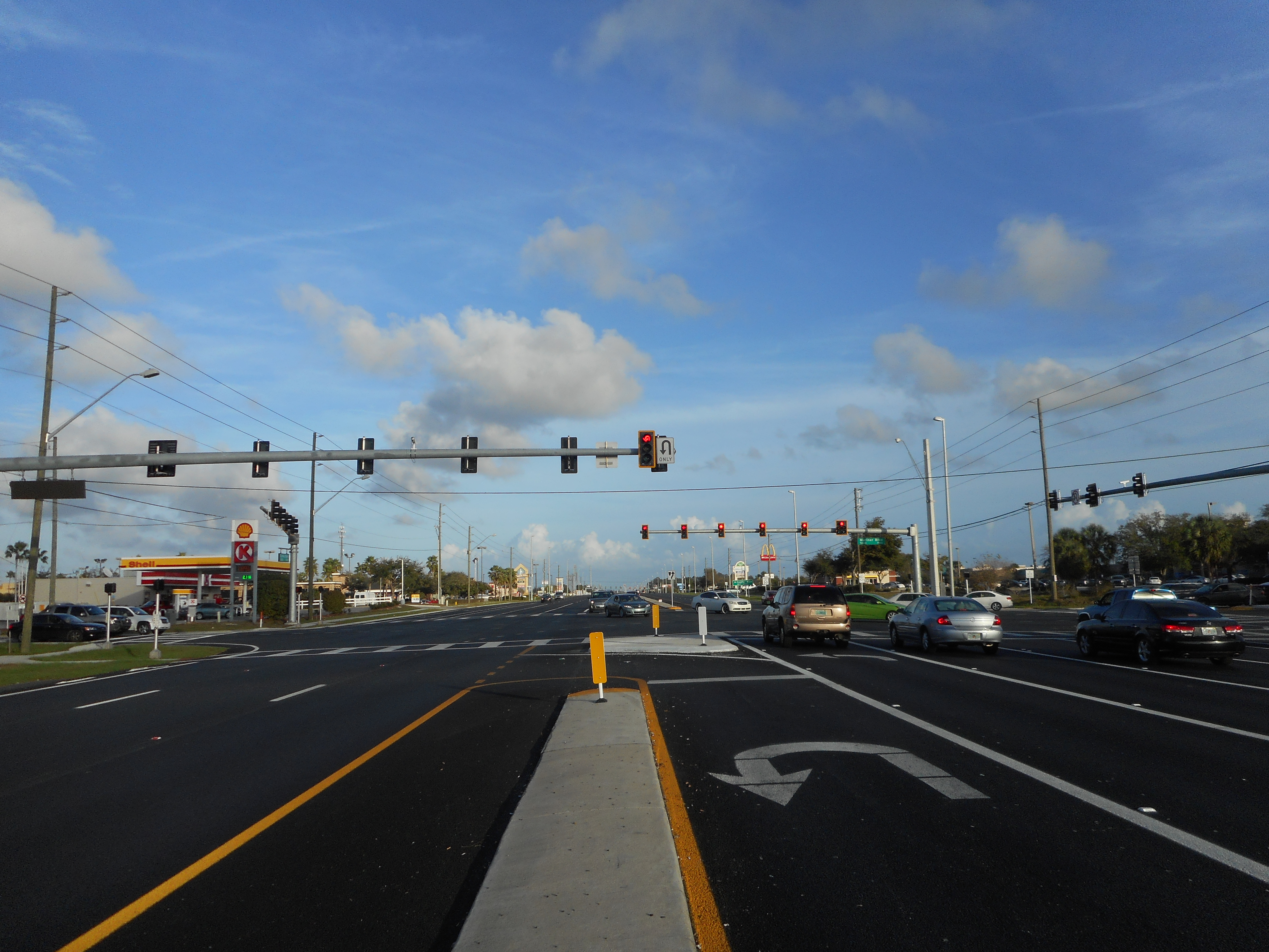Wide multi-lane road at a signalized intersection with overhead traffic signals and turn lanes.