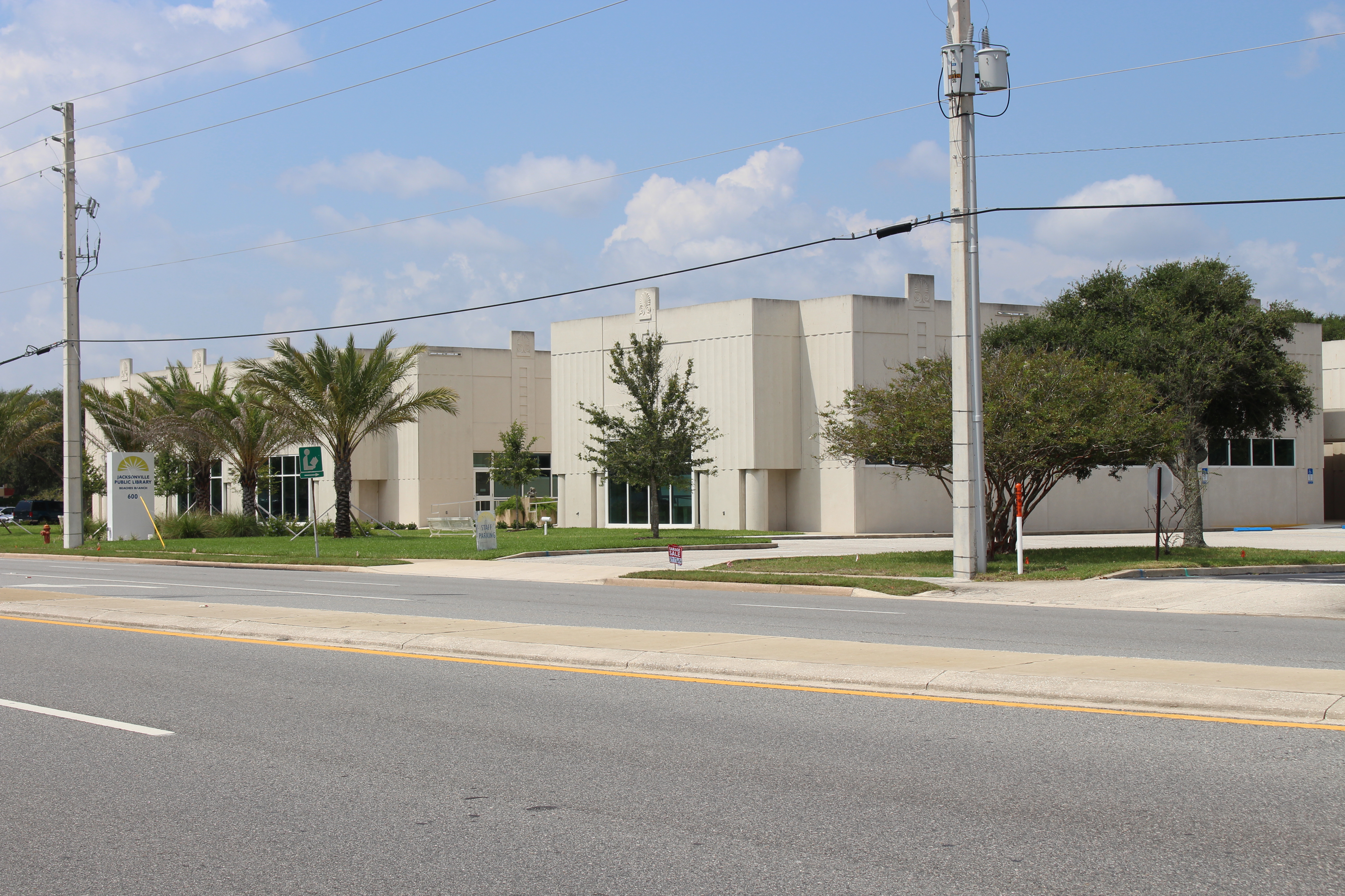 Low-rise beige library building with palm trees along the front on a sunny day.