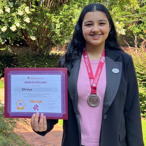 Smiling girl in a black blazer holding a framed award certificate and wearing a silver medal on a red lanyard.