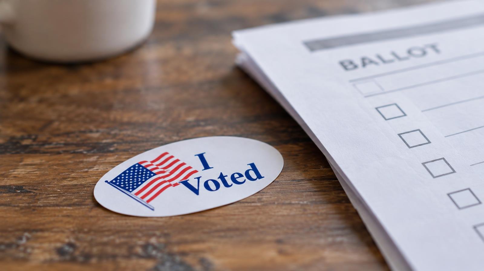 A white 'I Voted' sticker with an American flag design beside a folded ballot.