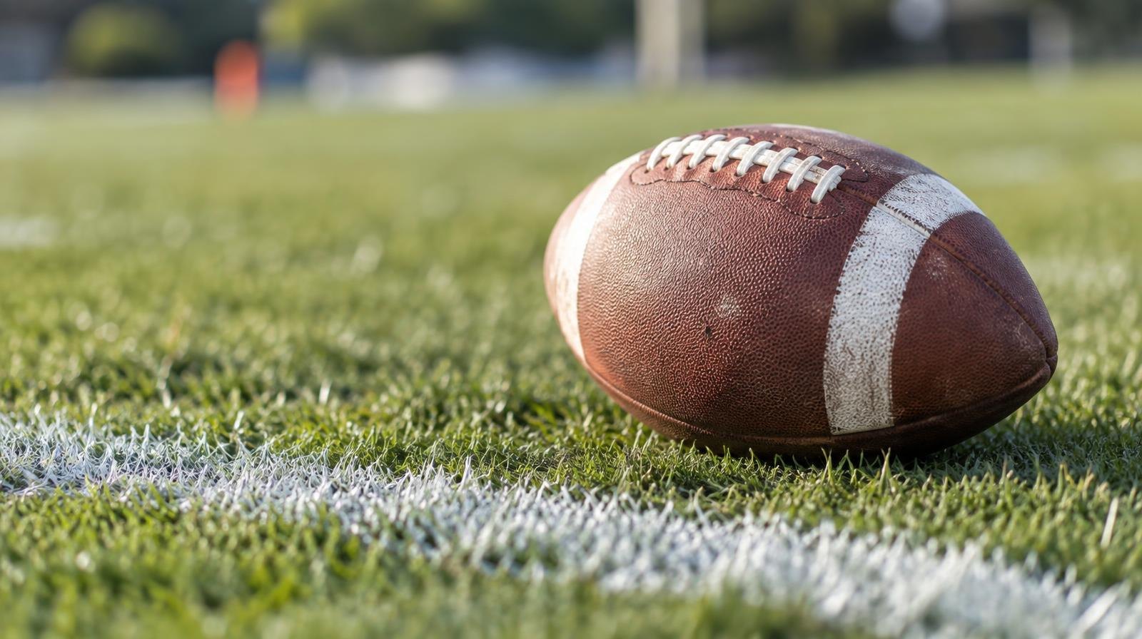An American football resting on green grass beside a white yard line.