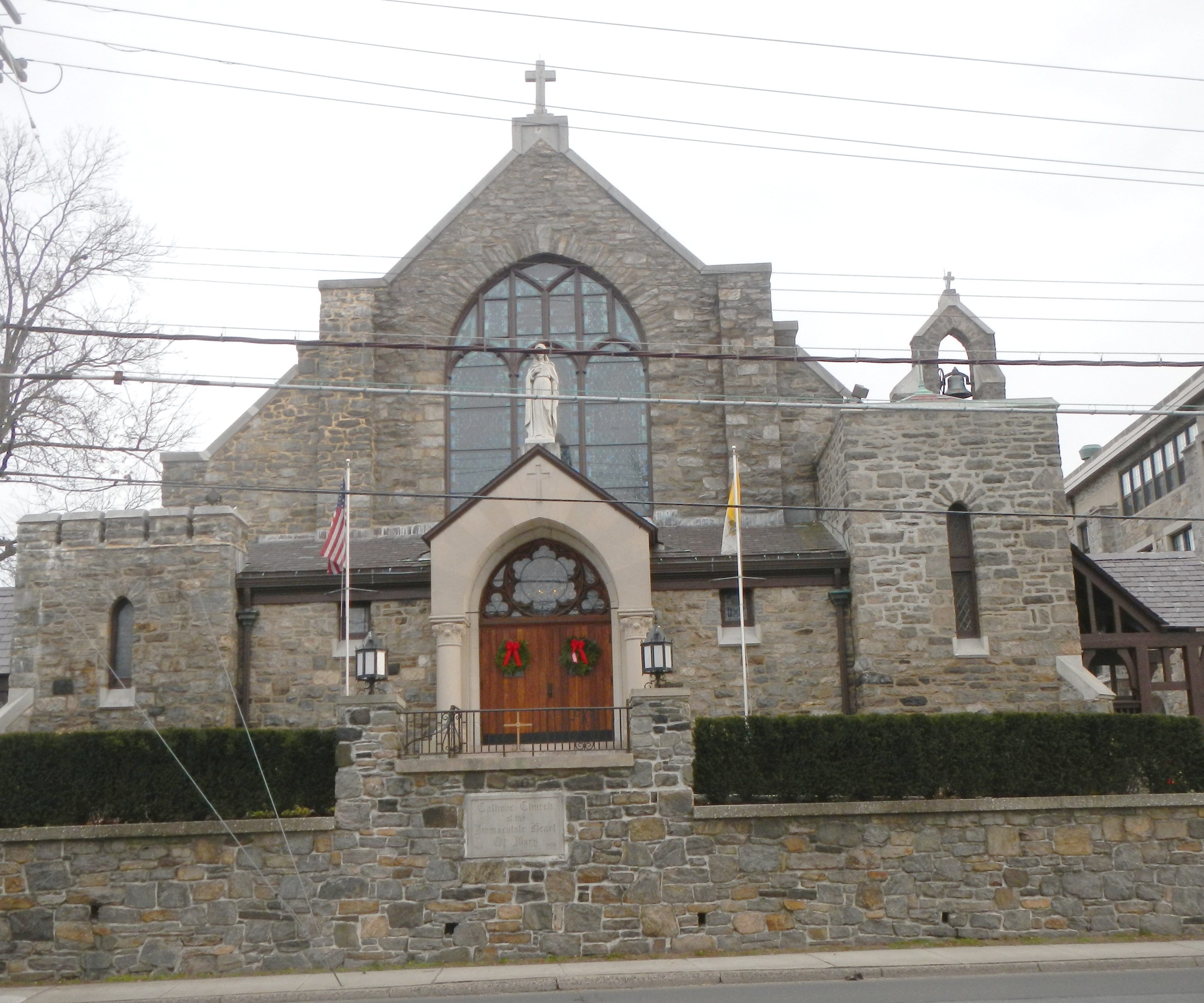 Stone Catholic church with a cross on the gable and a statue above the entrance doors.