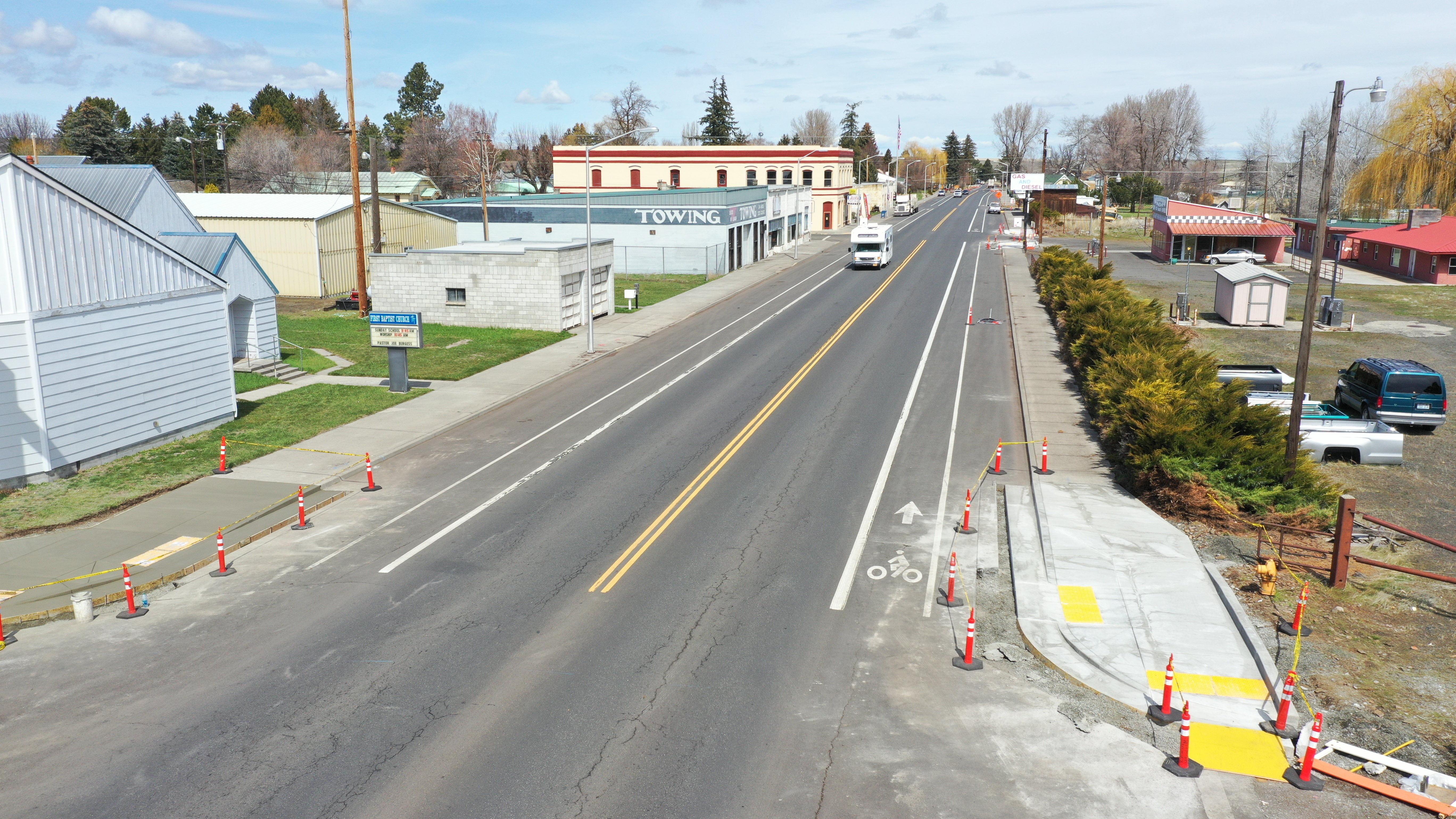 Orange traffic cones line a road beside freshly poured concrete curb ramps during construction.