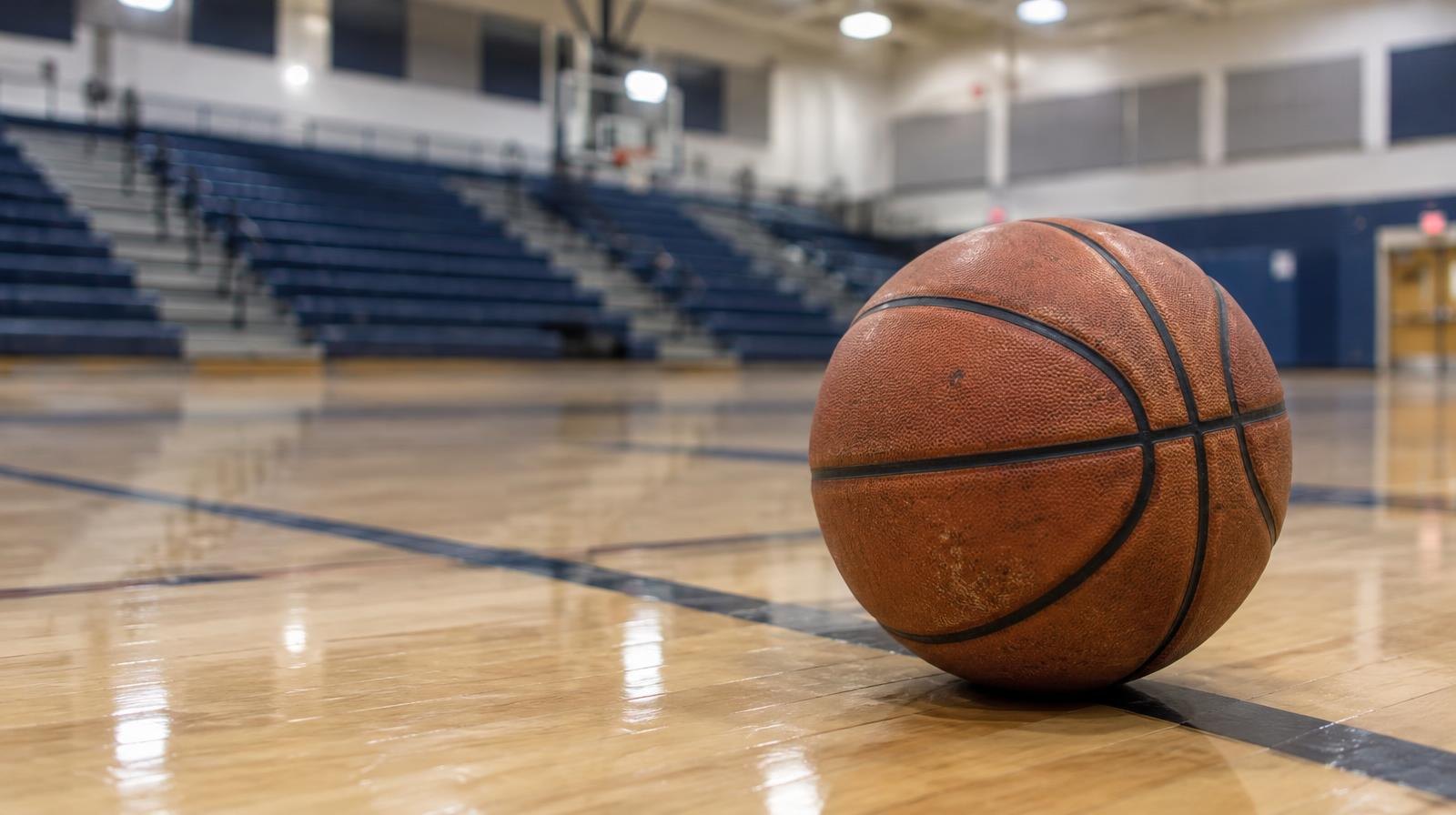 A basketball resting on a hardwood gymnasium floor near the center court line.