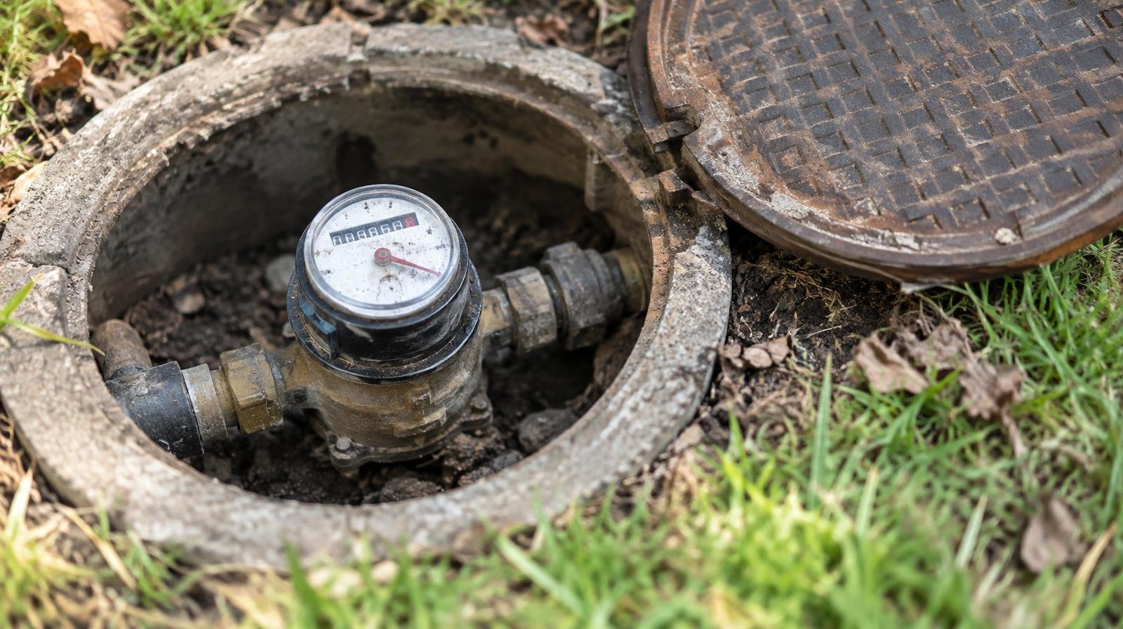 Residential water meter in an open concrete pit showing dial face and pipe connections.
