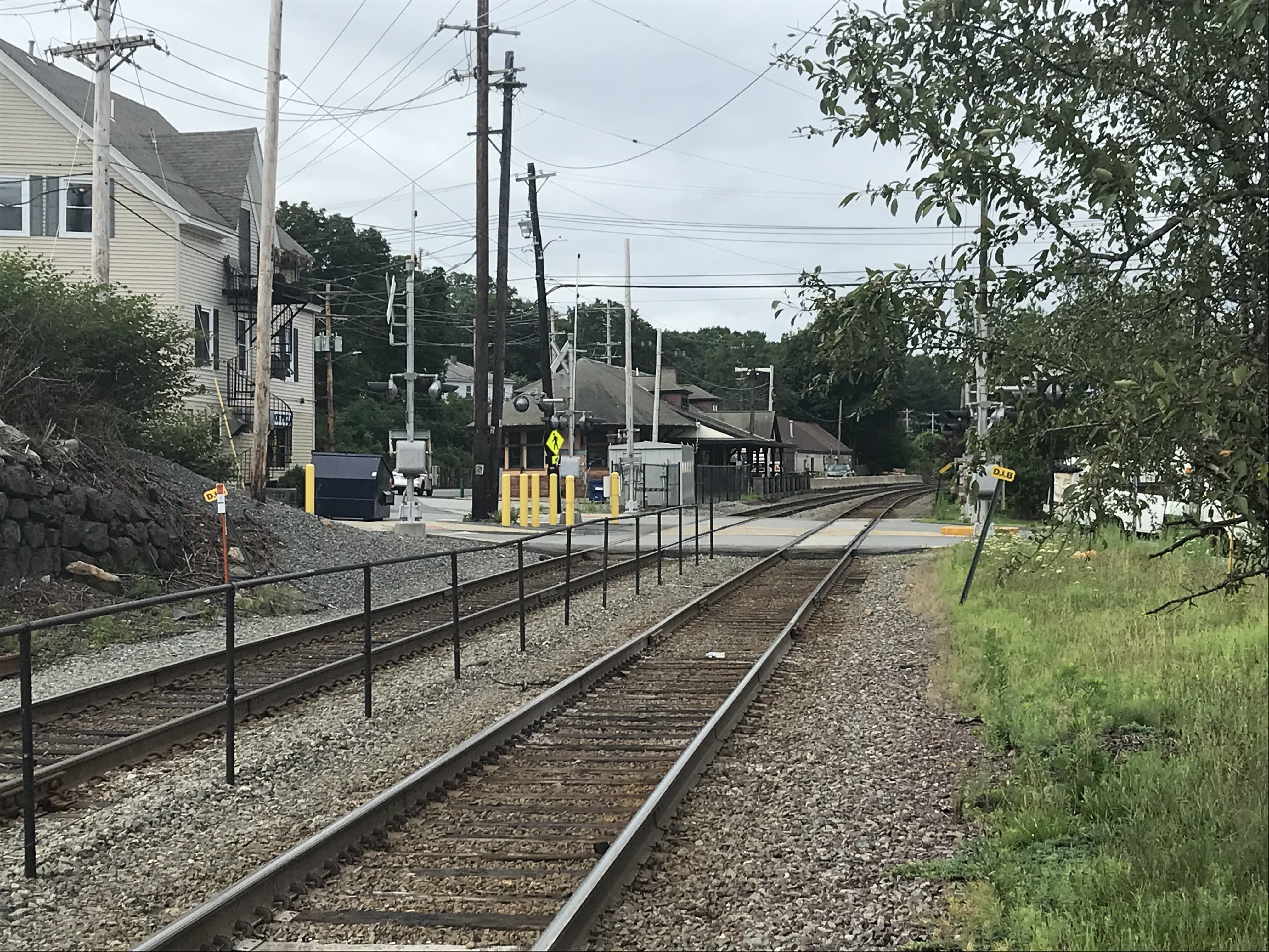 Railroad tracks bisect a three-way road intersection near a commuter rail station platform.