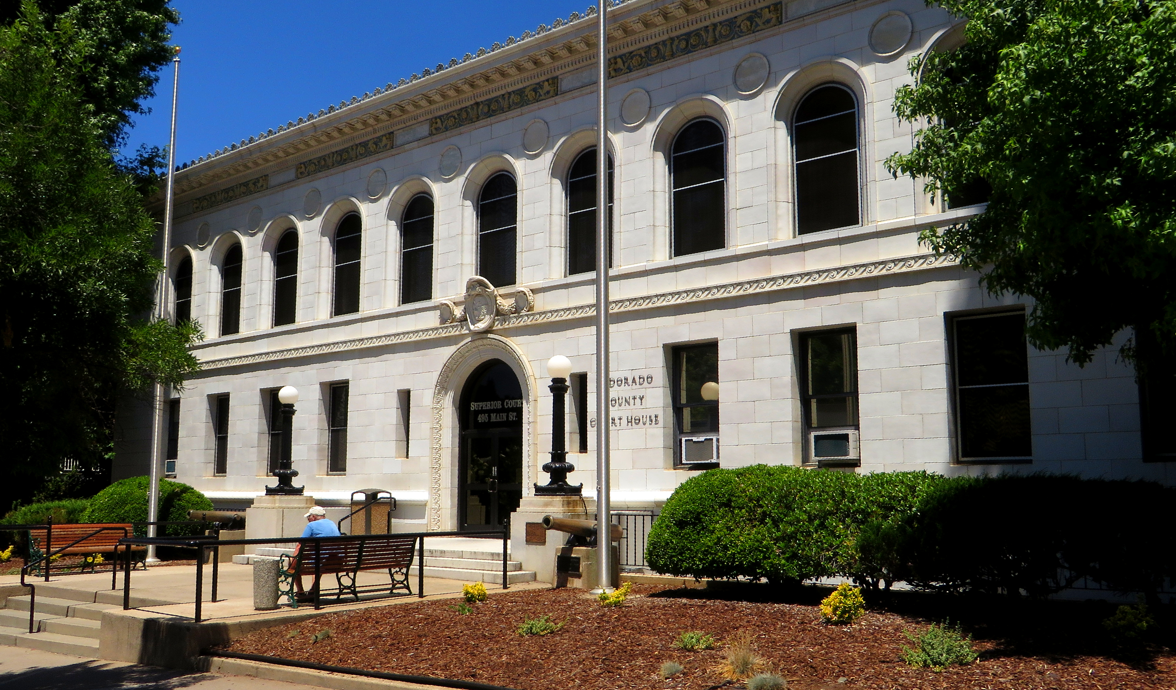 Neoclassical stone courthouse building with arched windows and landscaped grounds.