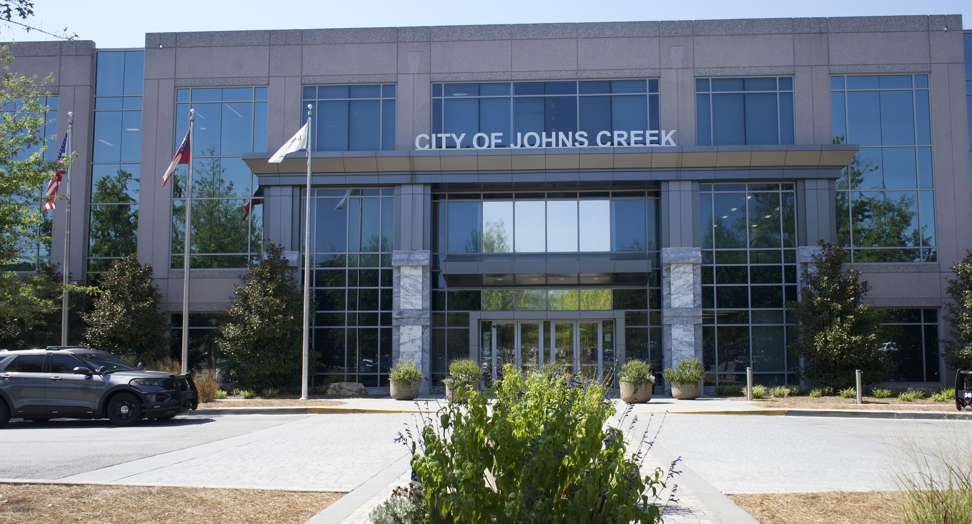 Modern glass-and-brick municipal building exterior with three flagpoles out front.