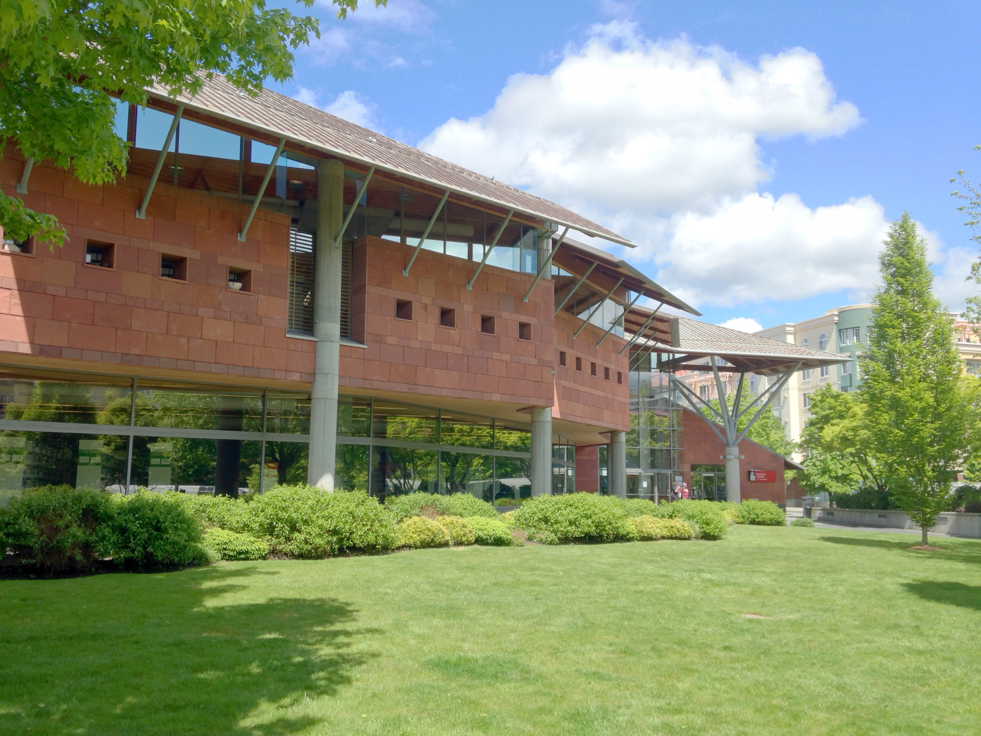 Exterior of a modern red-brick library building with large glass windows and a green lawn.