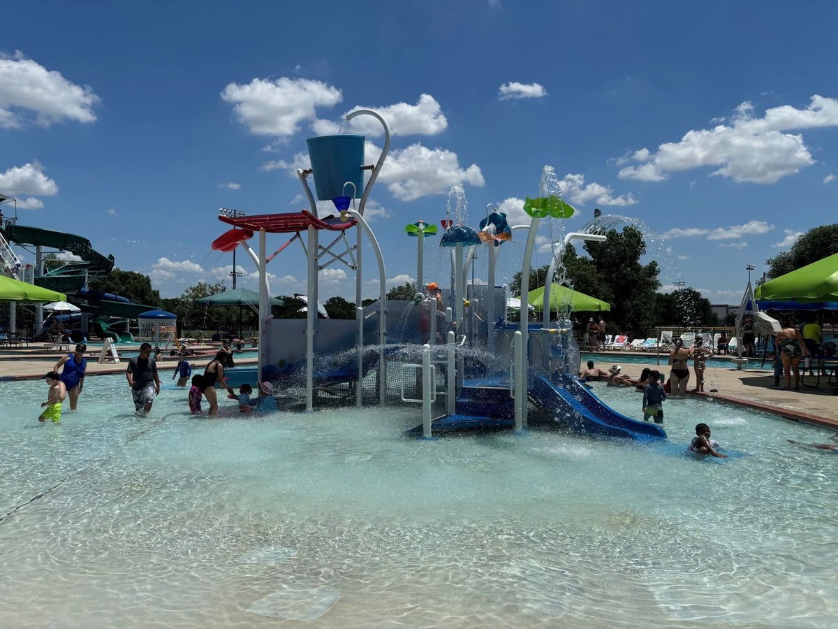 Children play around a multi-level outdoor water park structure with slides and spray features.
