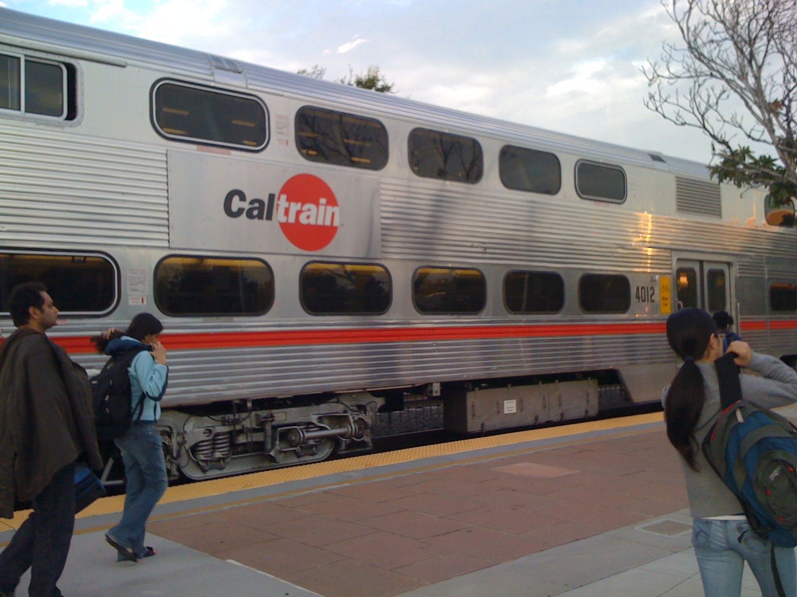 Passengers stand on a platform next to a silver Caltrain double-decker passenger car.