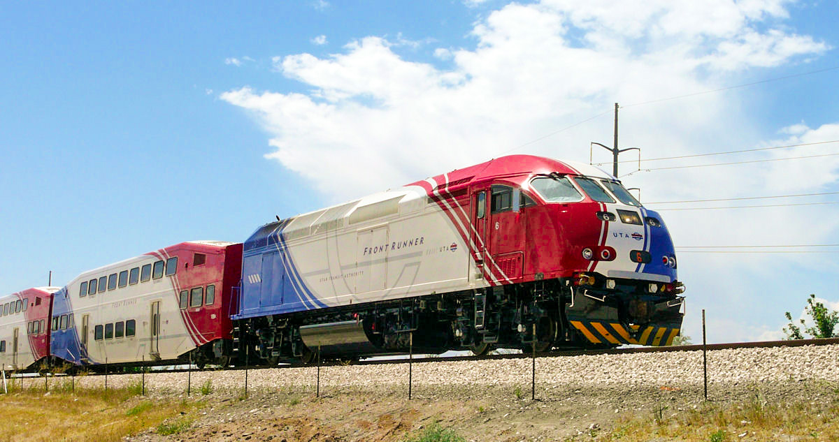 A red, white, and blue commuter train travels along a rail line through an arid landscape.