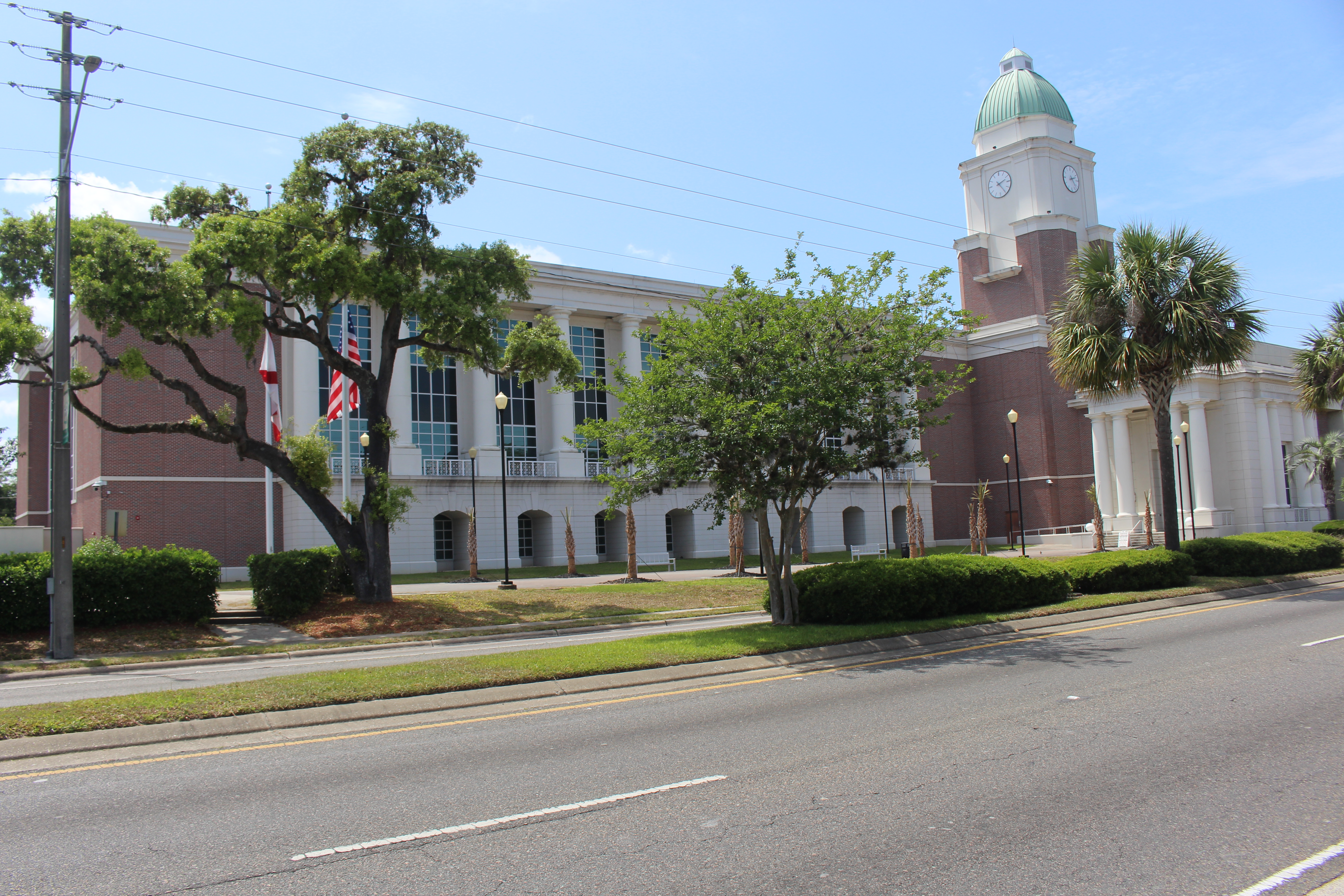 Brick courthouse with white columns, green-domed clock tower, flags, and palm trees.