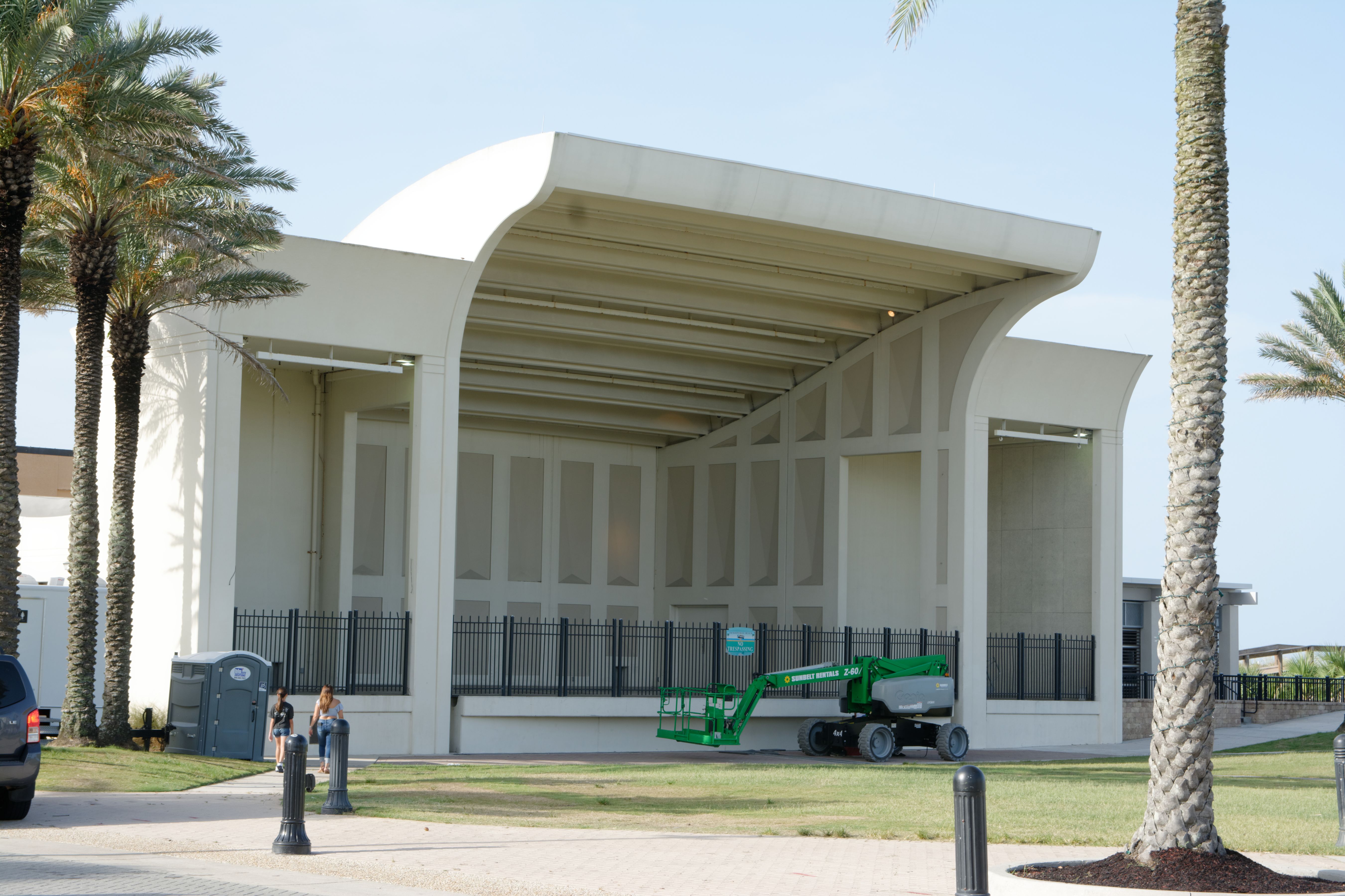 Open-air pavilion with curved white canopy roof surrounded by palm trees.