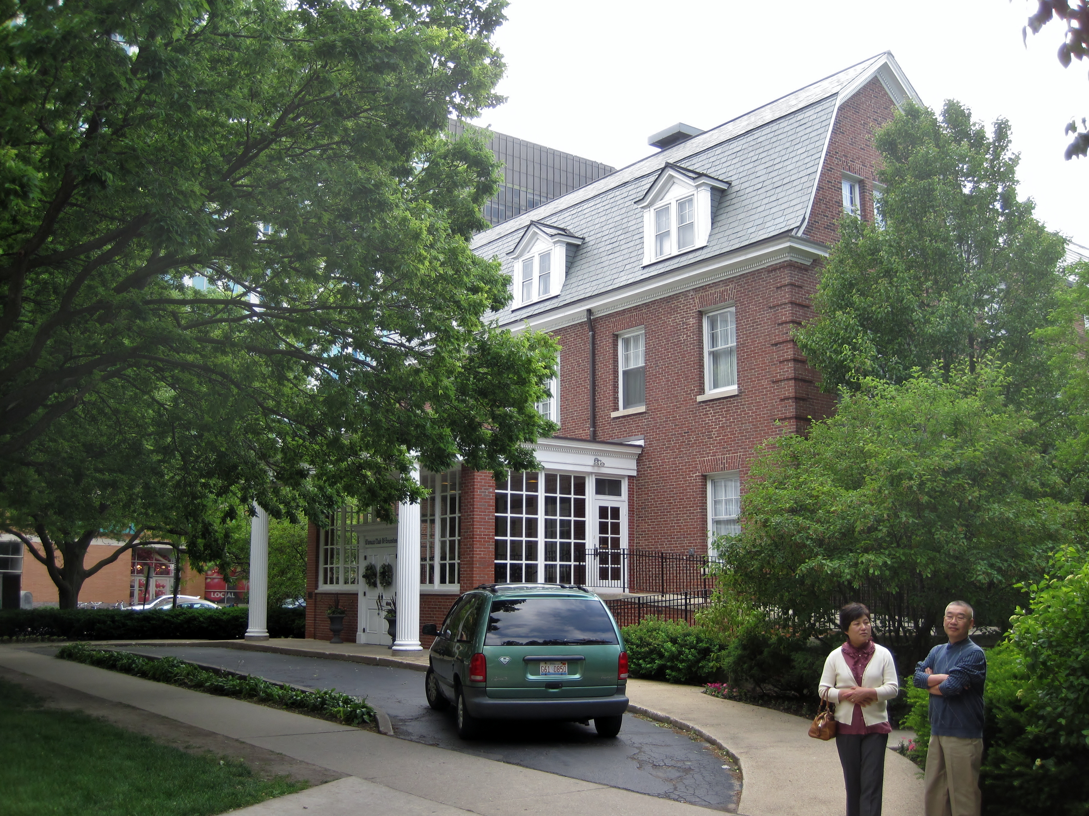 Two-story red brick building with a slate roof and white columned entrance, surrounded by trees.