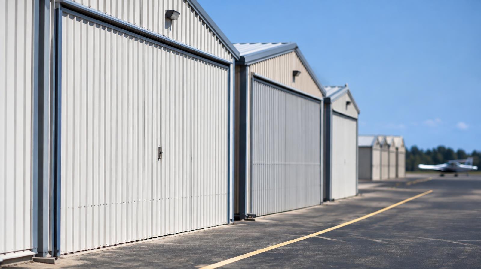 Row of small aircraft T-hangars with closed metal doors on a sunny tarmac.