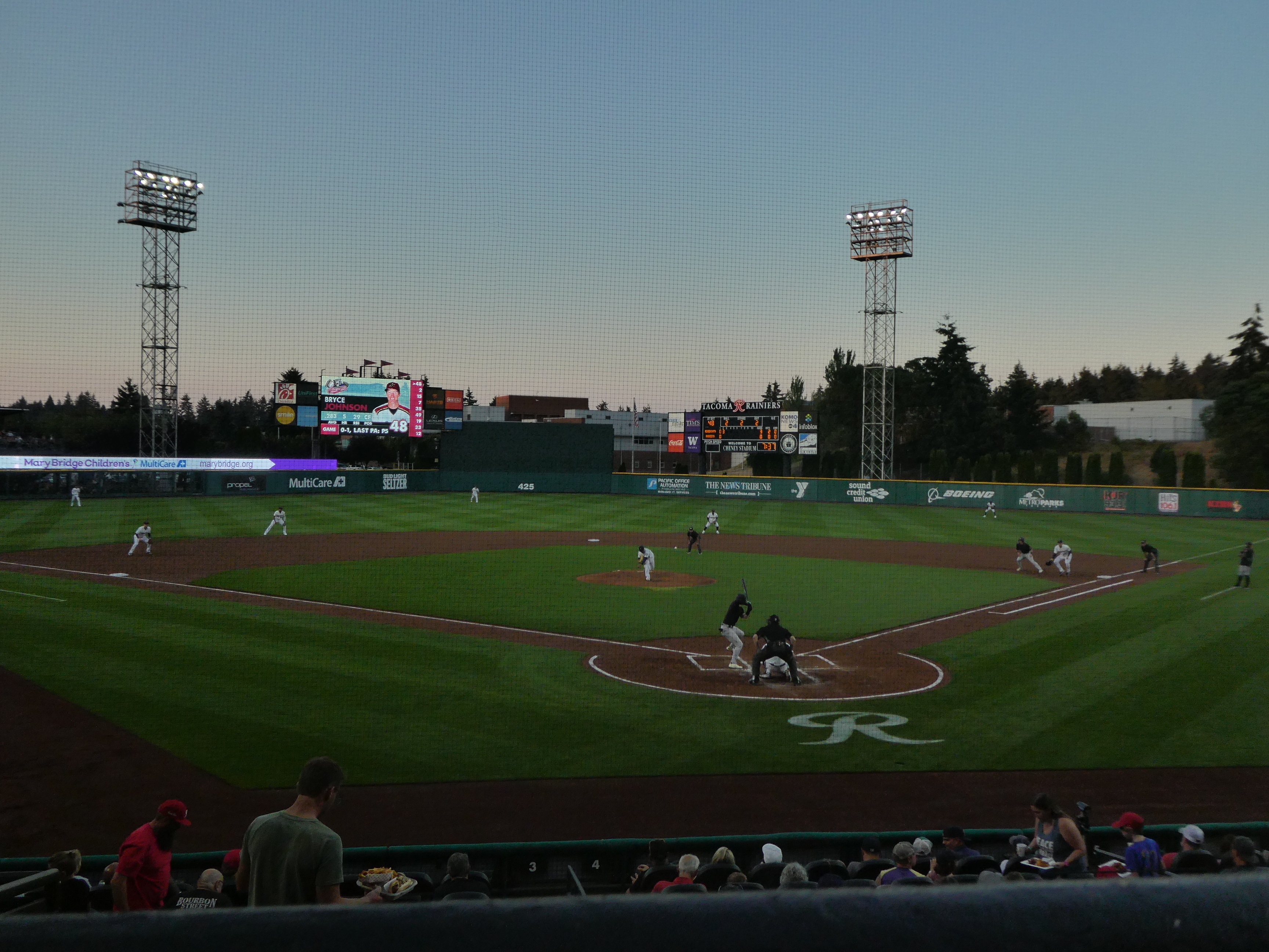 Baseball game in progress at a stadium viewed from the stands at dusk.