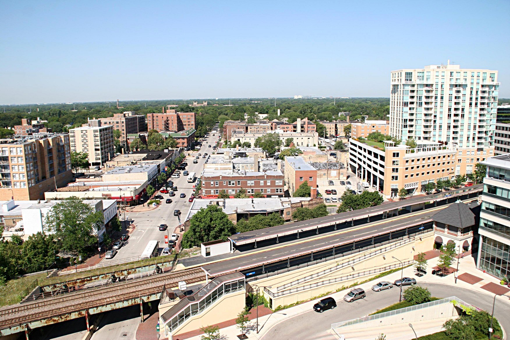 Aerial view of a downtown commercial street with shops, a rail station, and tree-lined blocks.