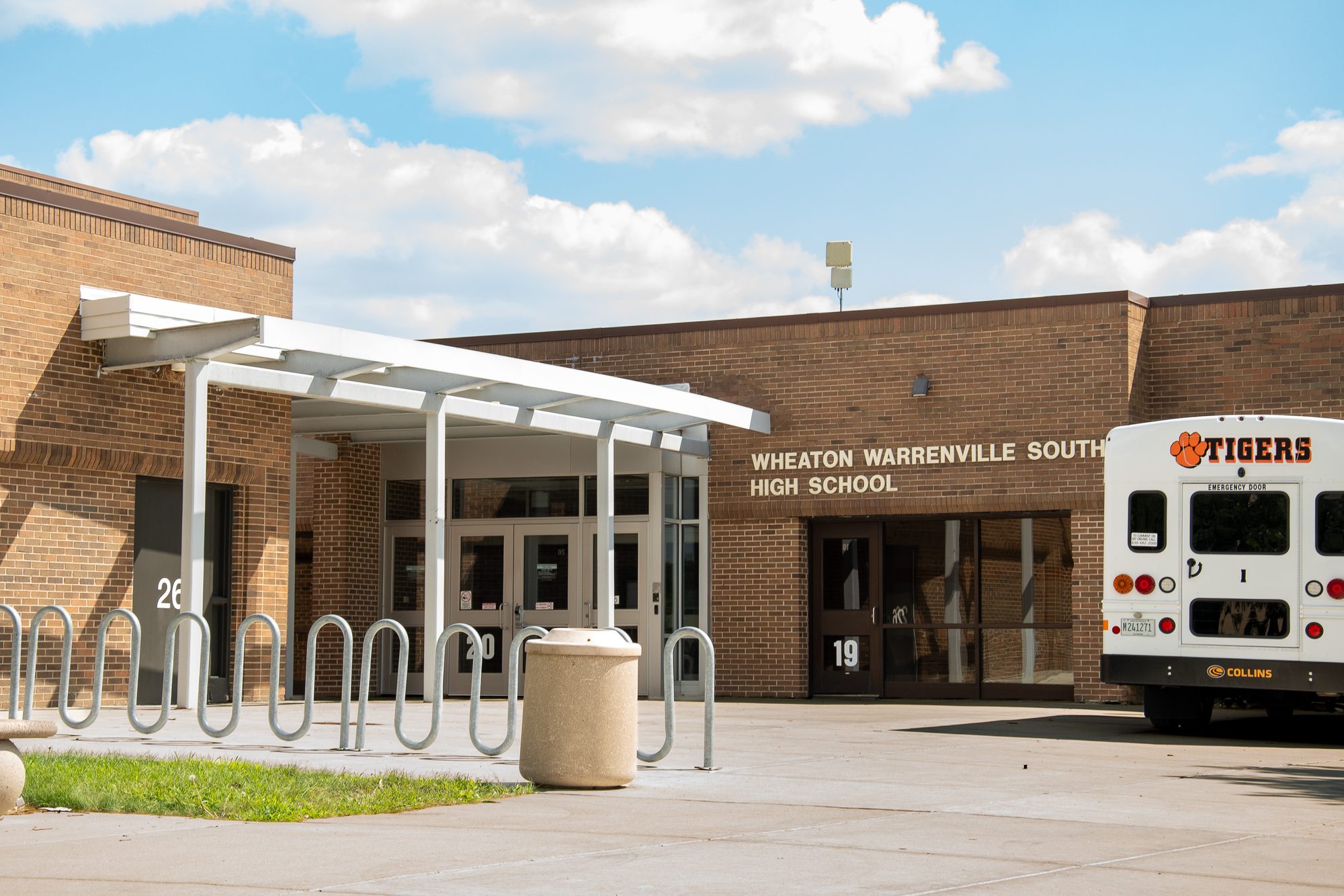 Brick high school entrance with covered bike rack and a parked school bus.