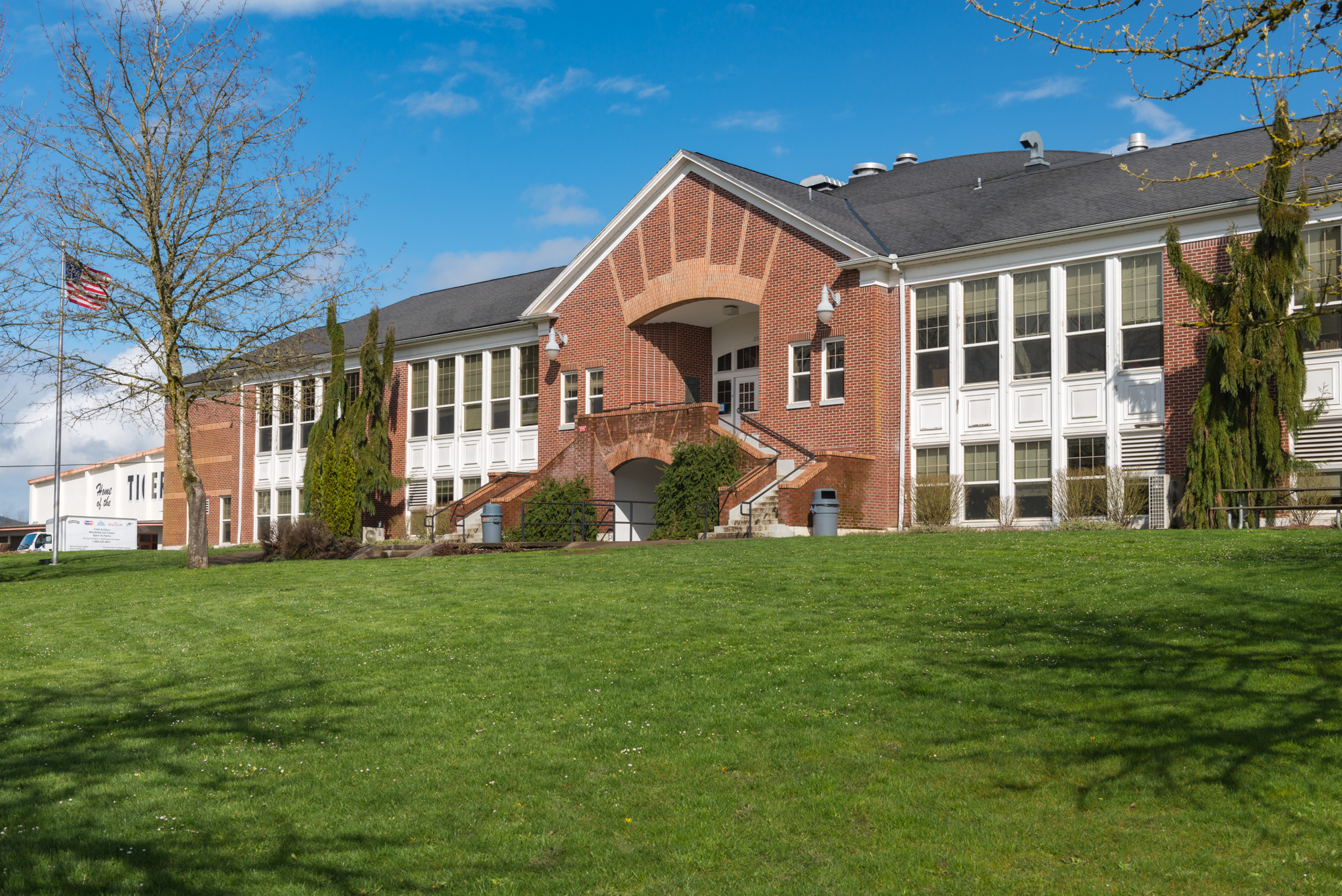 Two-story red brick school building with a flagpole and green lawn.