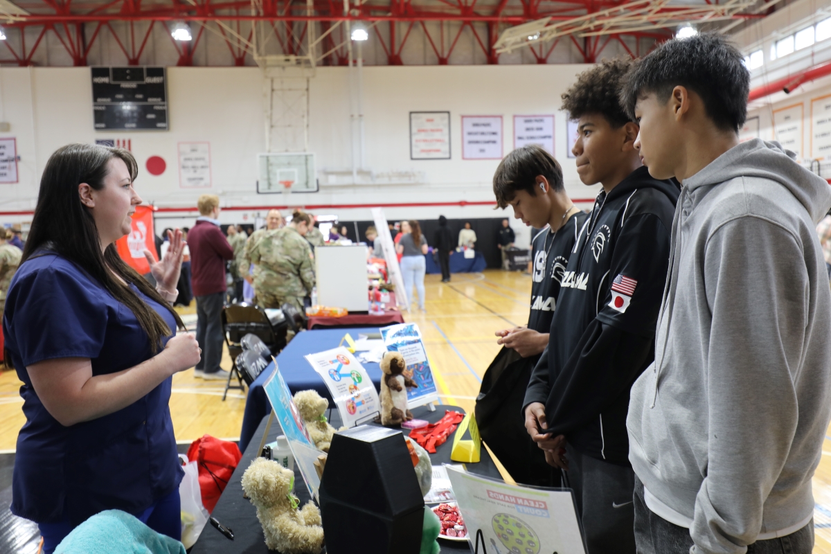 Students speaking with a booth representative at a college and career fair in a gymnasium.