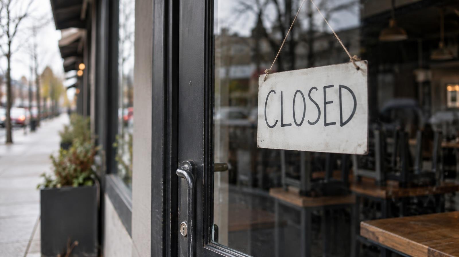 Darkened restaurant storefront with a closed sign hanging in the window.
