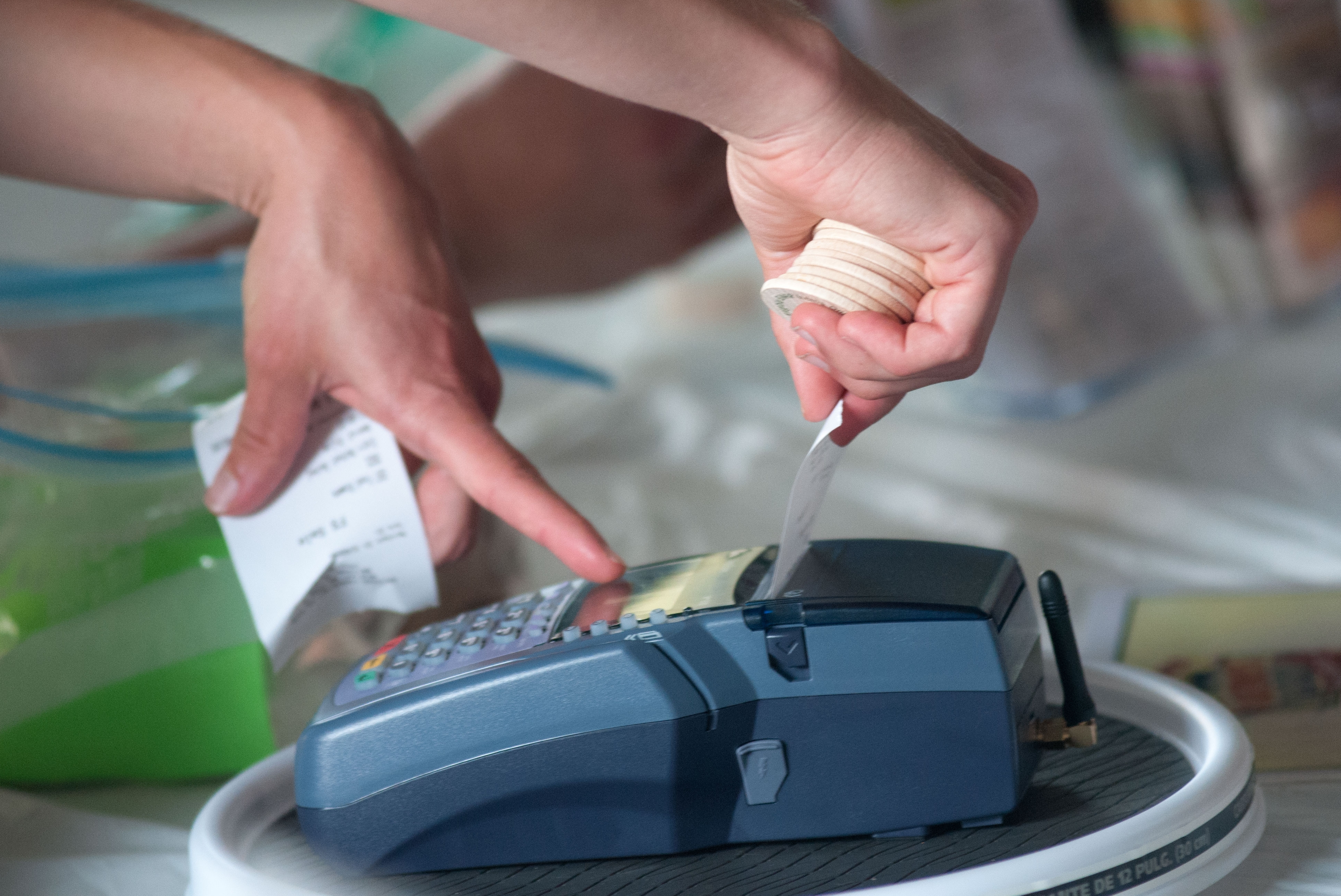 Hands operating a blue wireless card payment terminal and pulling a receipt.